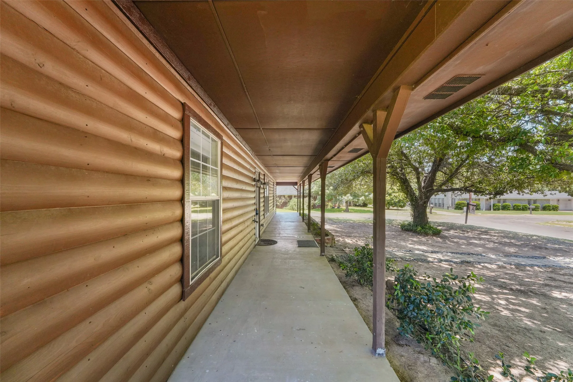 Expansive covered porch featuring a log cabin style exterior with multiple windows and a concrete pathway