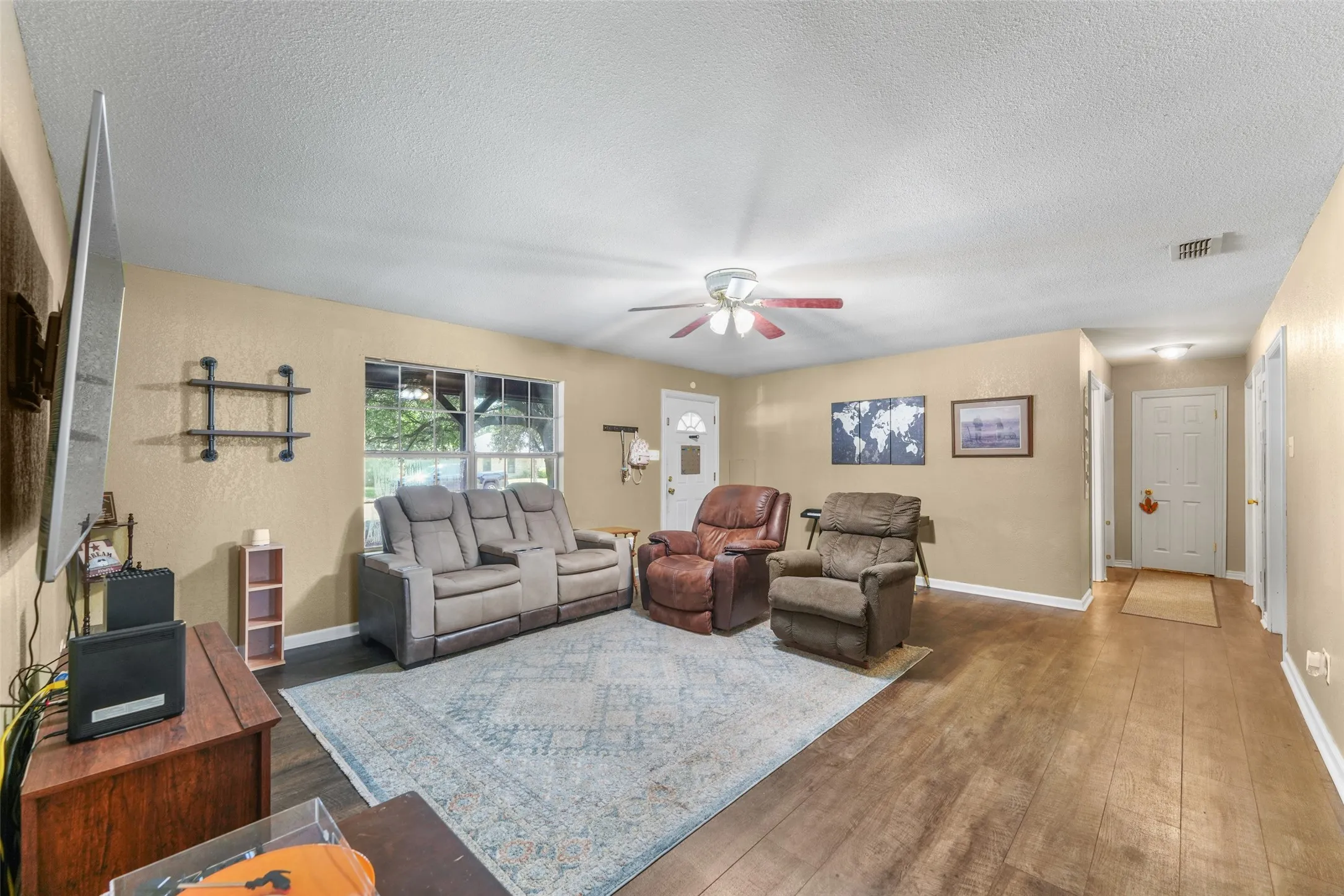 Spacious living area featuring wood-finish flooring, a ceiling fan, and ample natural light from multiple windows