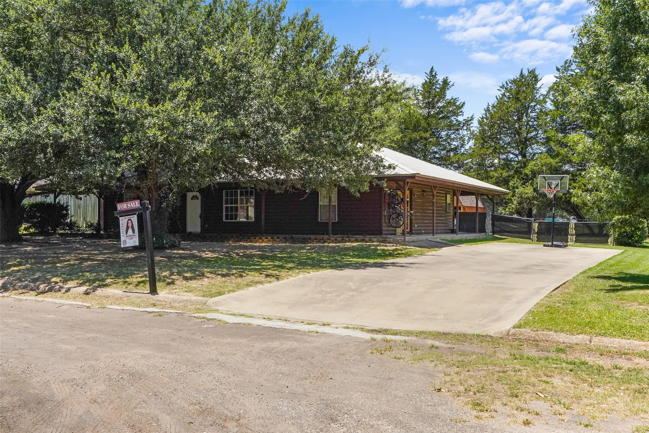 Ranch-style exterior with wood siding, a covered porch, a concrete driveway, and mature landscaping