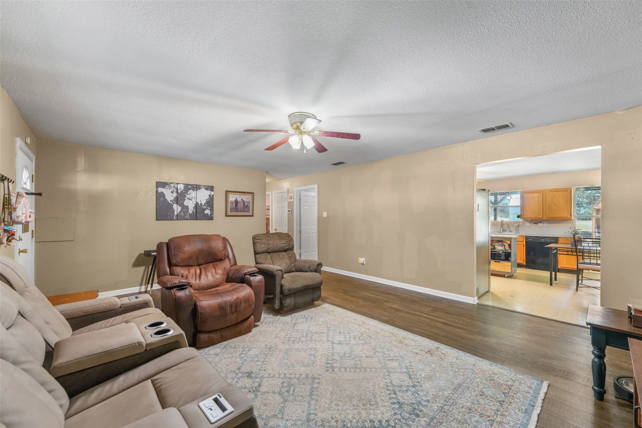 Spacious living area featuring wood-finish flooring, neutral wall tones, and a ceiling fan with integrated lighting