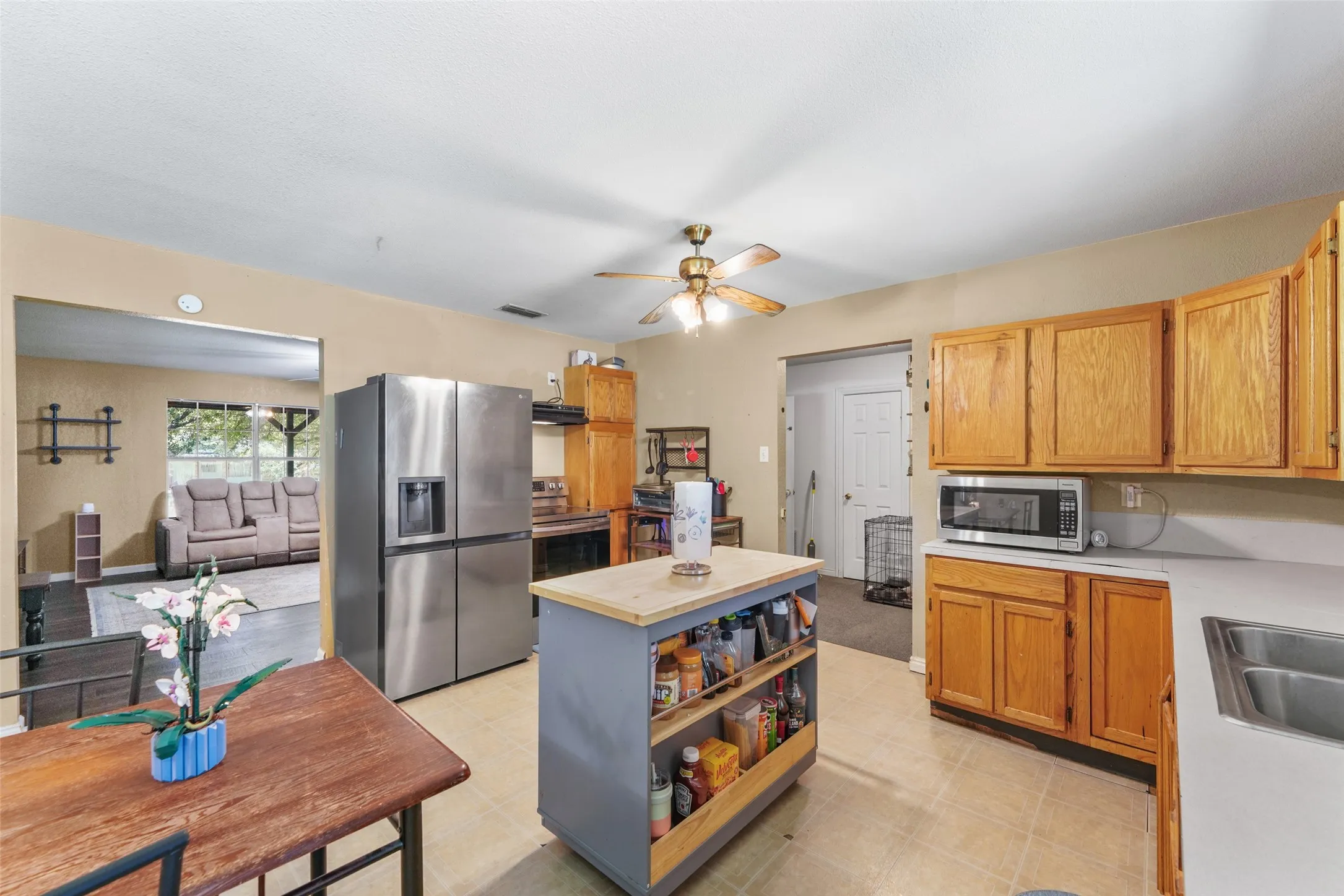 Kitchen featuring a stainless steel refrigerator, light wood-finish cabinetry, a built-in microwave, tile flooring, and a ceiling fan