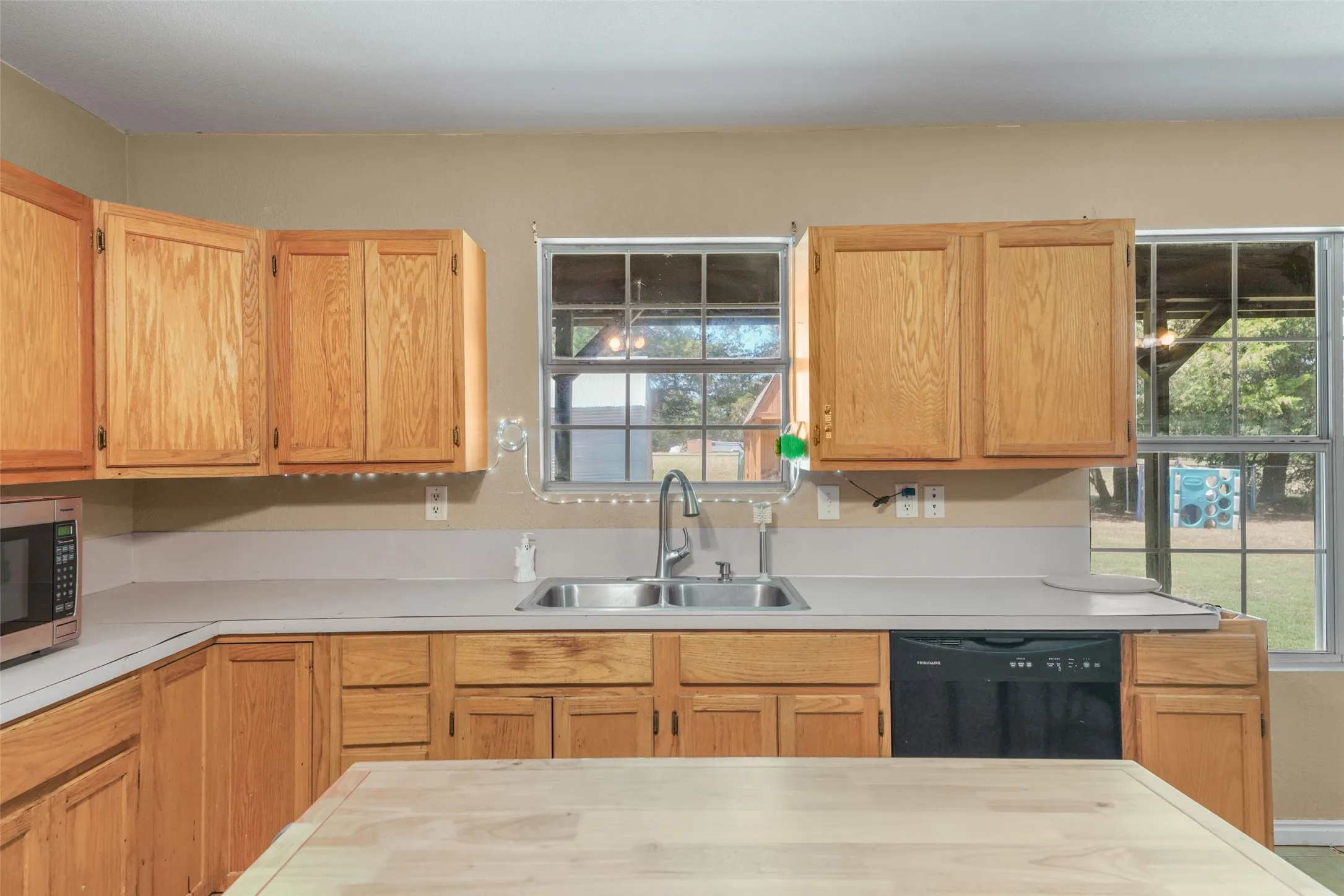 Kitchen featuring wood cabinetry, a dual-basin stainless steel sink, light-toned countertops, and a black dishwasher