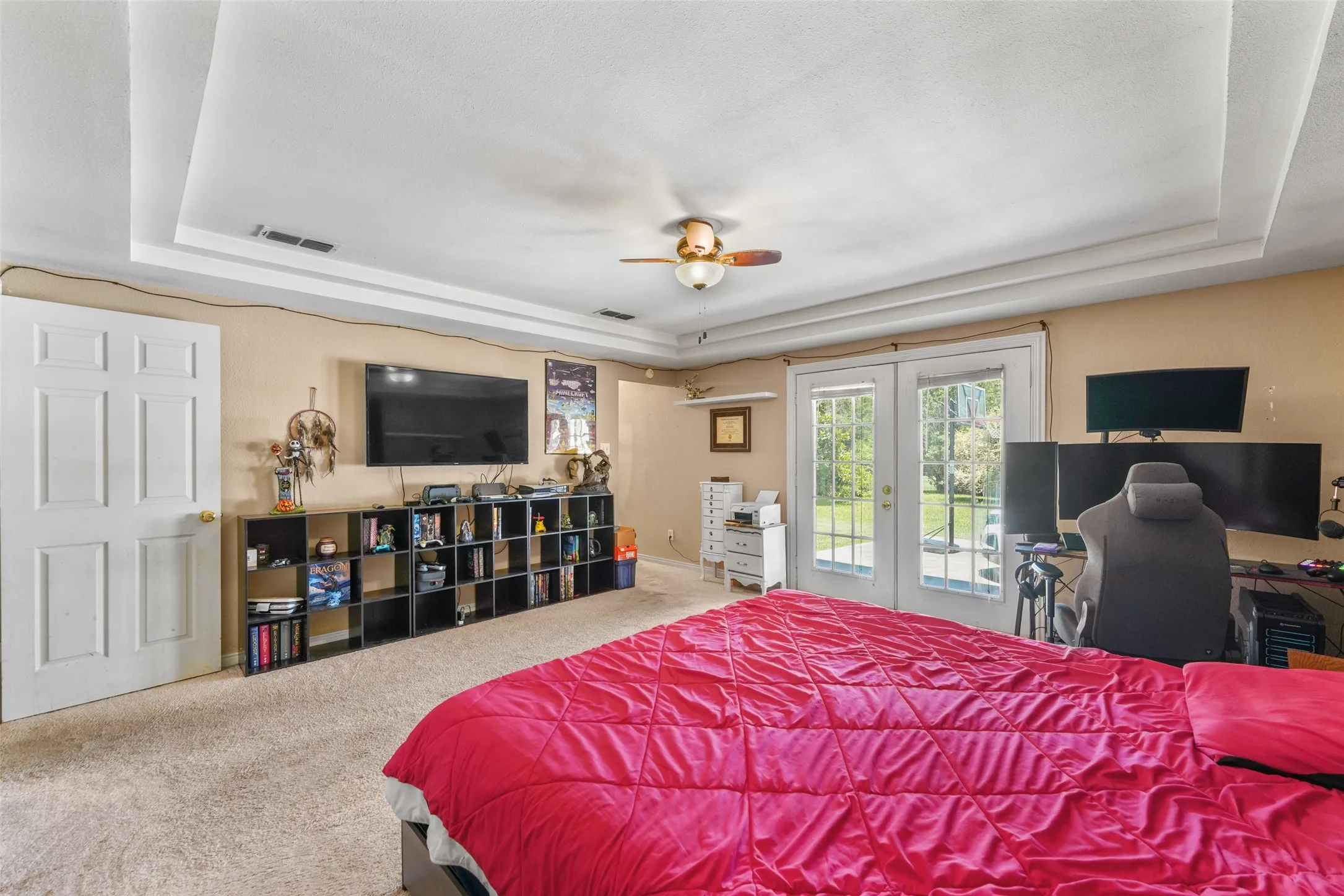 Spacious room featuring tray ceiling, ceiling fan, and light-colored carpet flooring