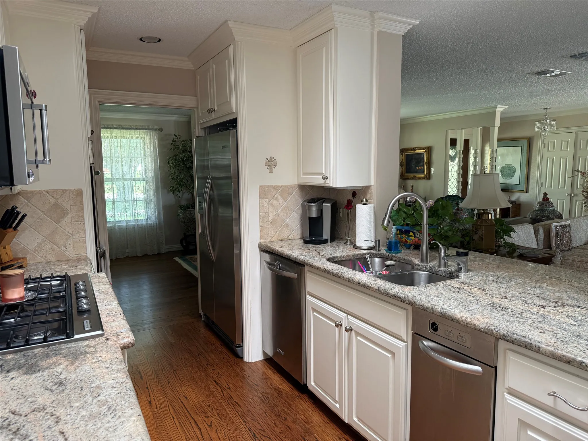 Kitchen featuring white cabinetry, granite countertops, hardwood flooring, and stainless steel appliances including a gas range and refrigerator