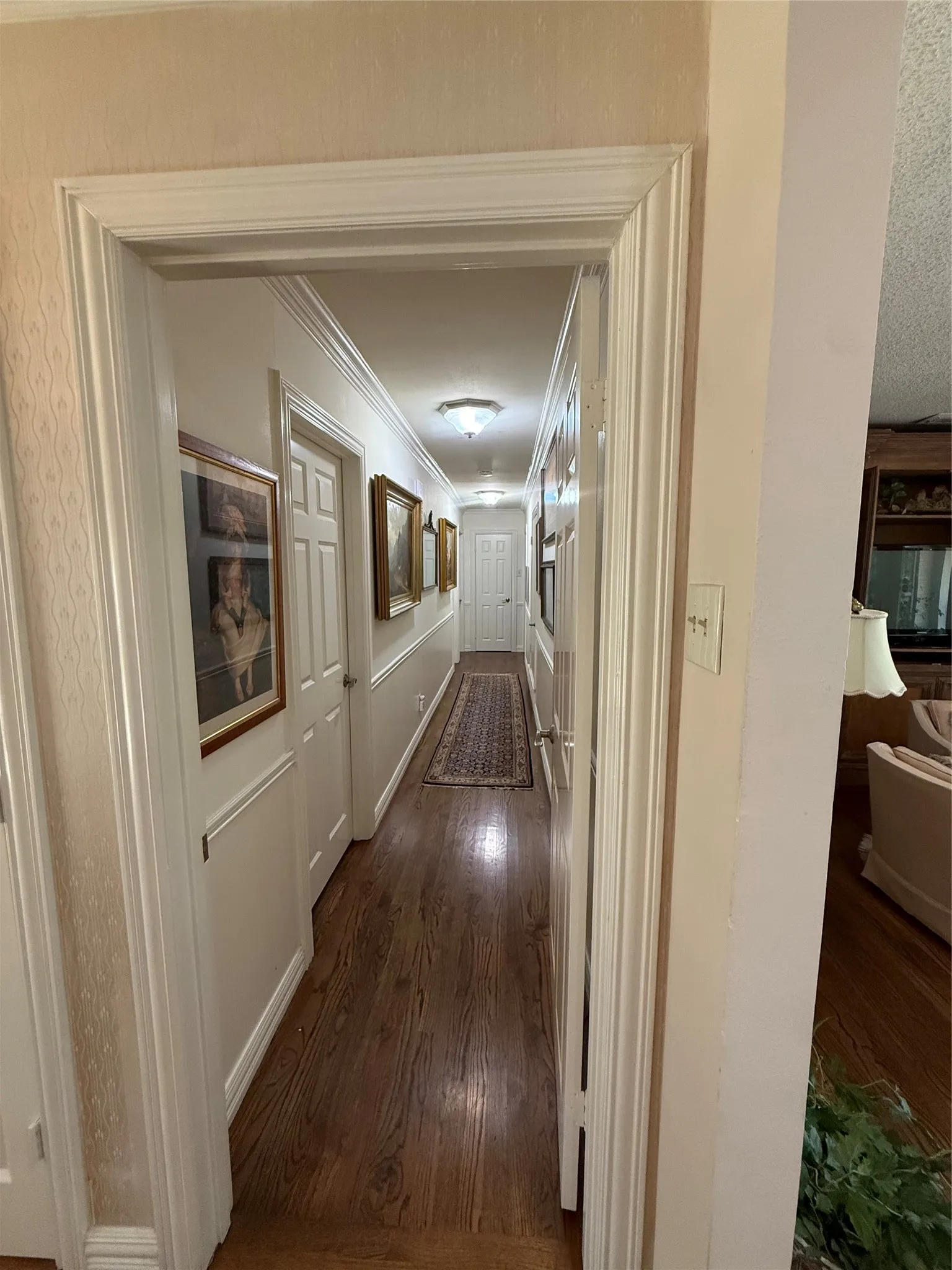 Hallway featuring wood-finish flooring, white crown molding, and white wainscoting