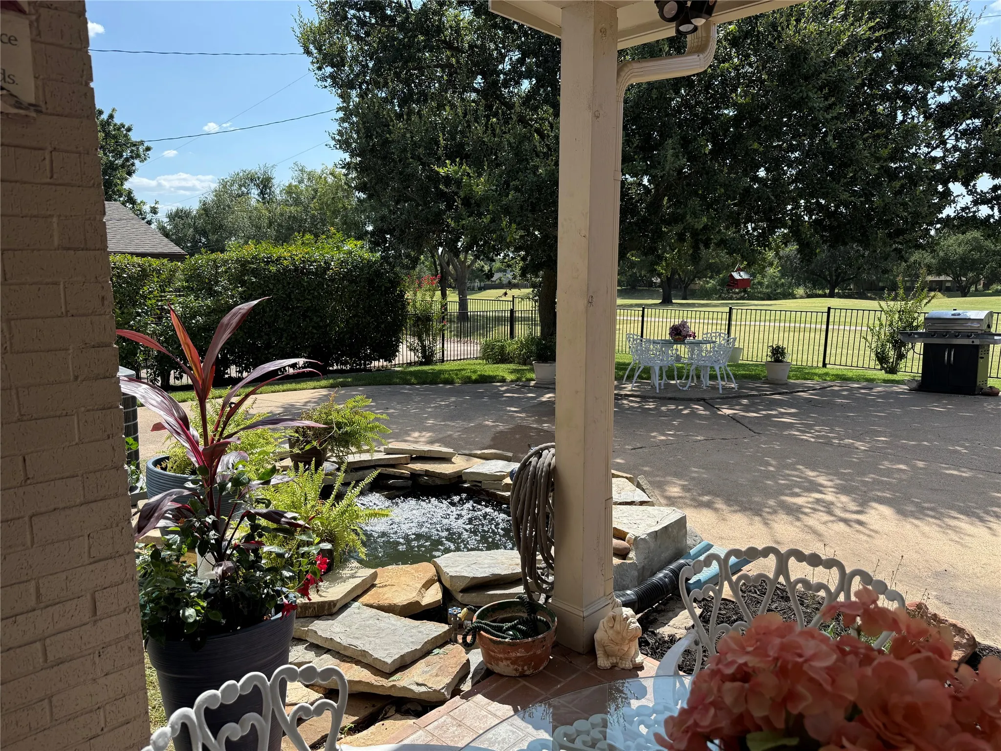 Covered patio featuring brick siding, a built-in water feature with stone accents, and an expansive paved area