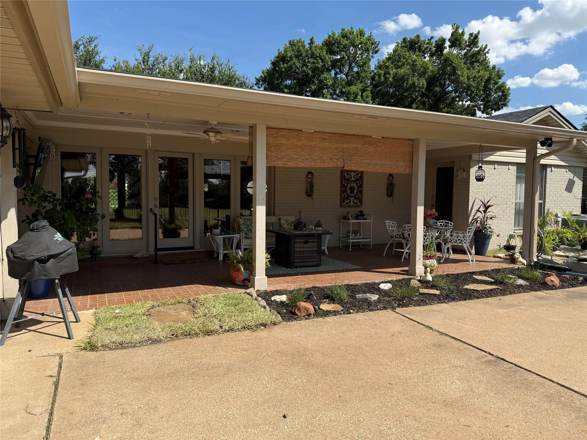 Expansive covered patio featuring a brick paver surface, ceiling fan, recessed lighting, and a landscaped garden bed
