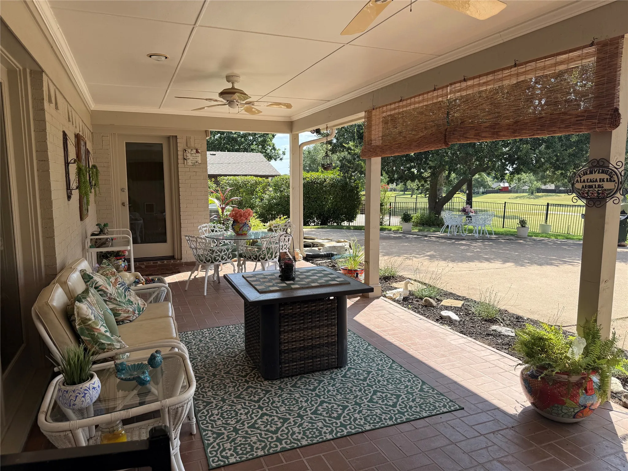 Expansive covered patio featuring a brick-patterned floor, two ceiling fans, a full-lite glass door, and a woven roller shade
