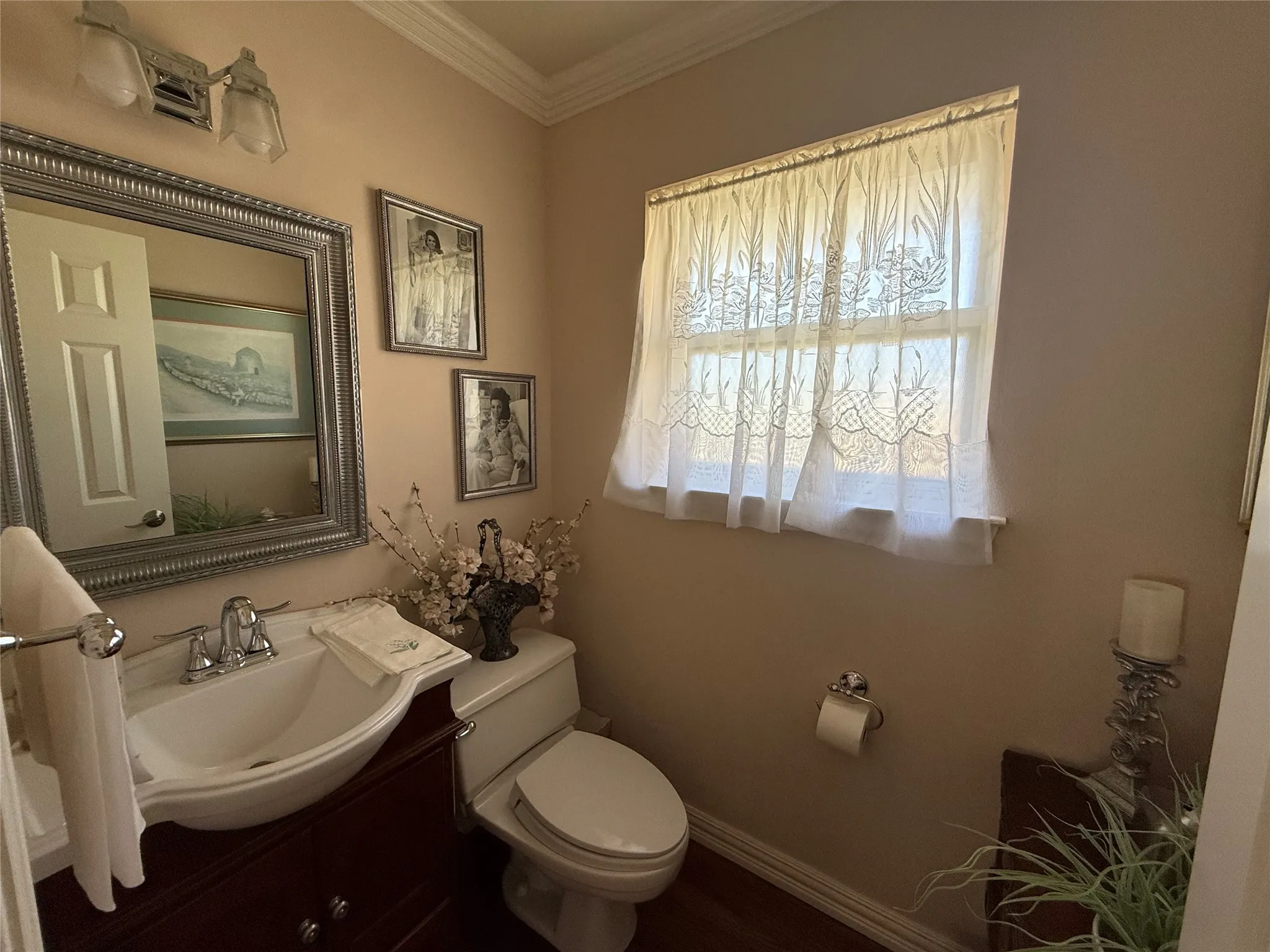 Powder room featuring a dark wood-finish vanity with a white vessel sink, a silver-framed mirror, crown molding, and wood-finish flooring