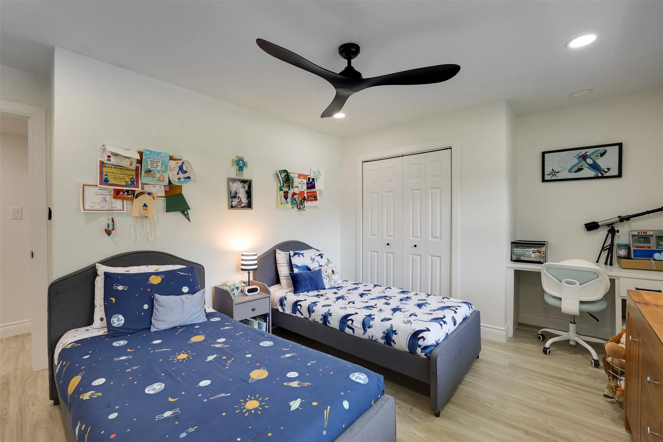 Bright bedroom featuring light wood-finish flooring, a contemporary black ceiling fan, recessed lighting, and a bi-fold door closet