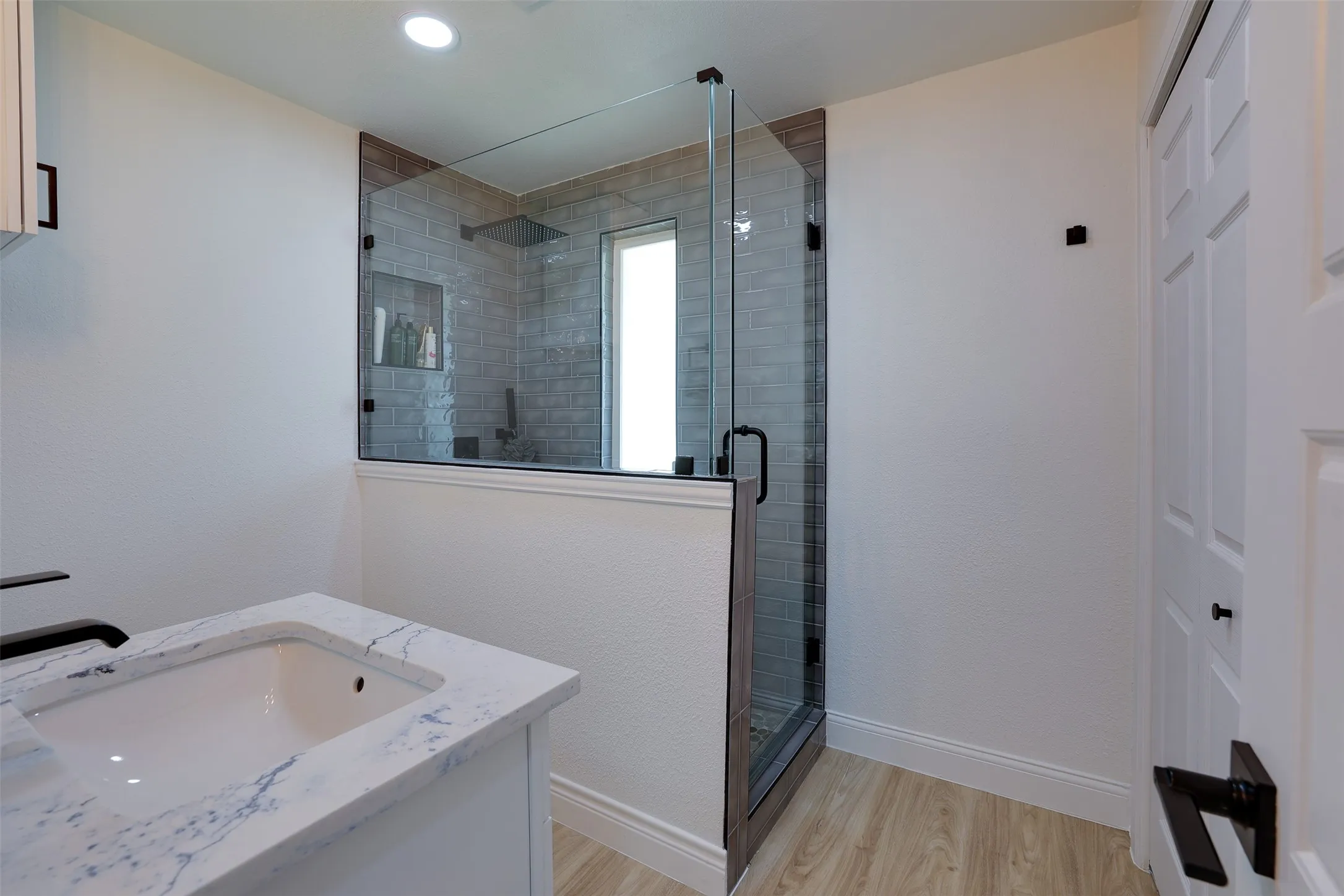 Modern bathroom featuring a walk-in shower with glass enclosure and subway tile surround, a single vanity with a white countertop and rectangular sink, and wood-finish flooring