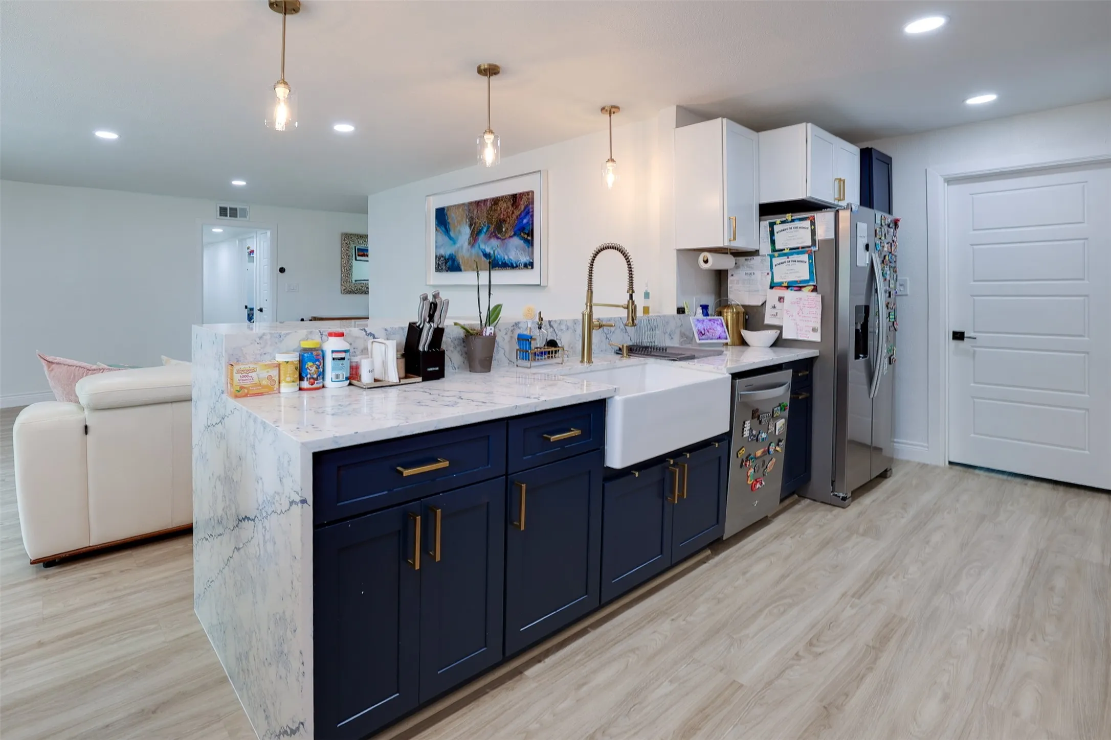 Kitchen island featuring a waterfall countertop with integrated farmhouse sink, brass-finish faucet, and deep blue cabinetry with brass-finish hardware