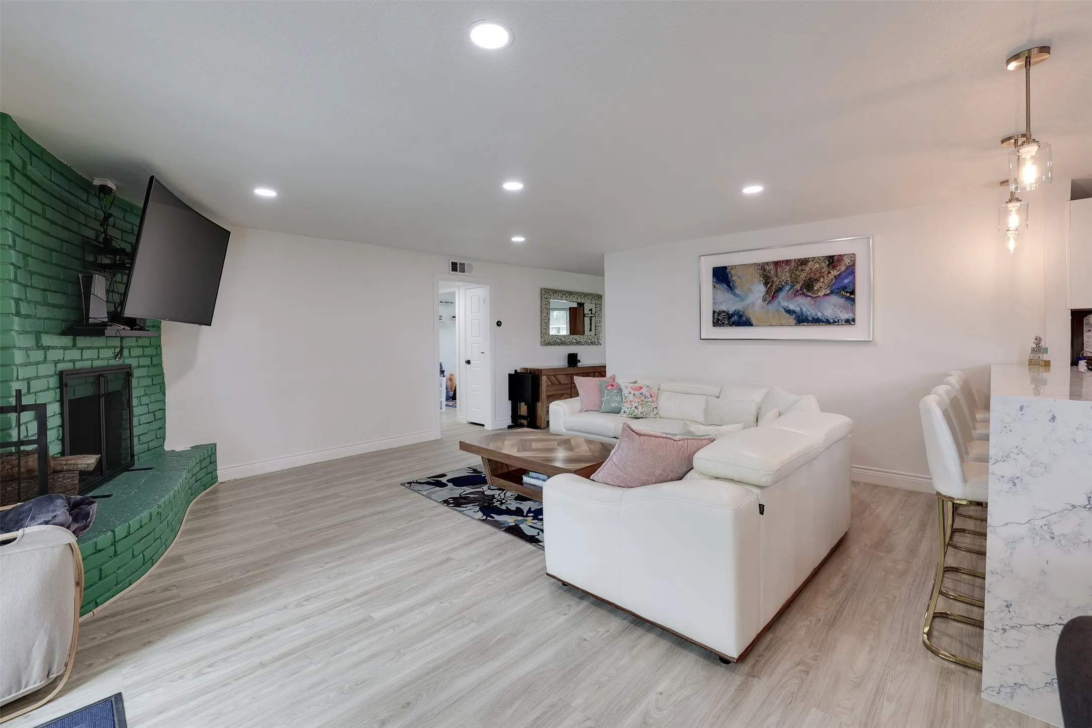 Open-concept living space featuring wood-finish flooring, recessed lighting, and a prominent brick fireplace