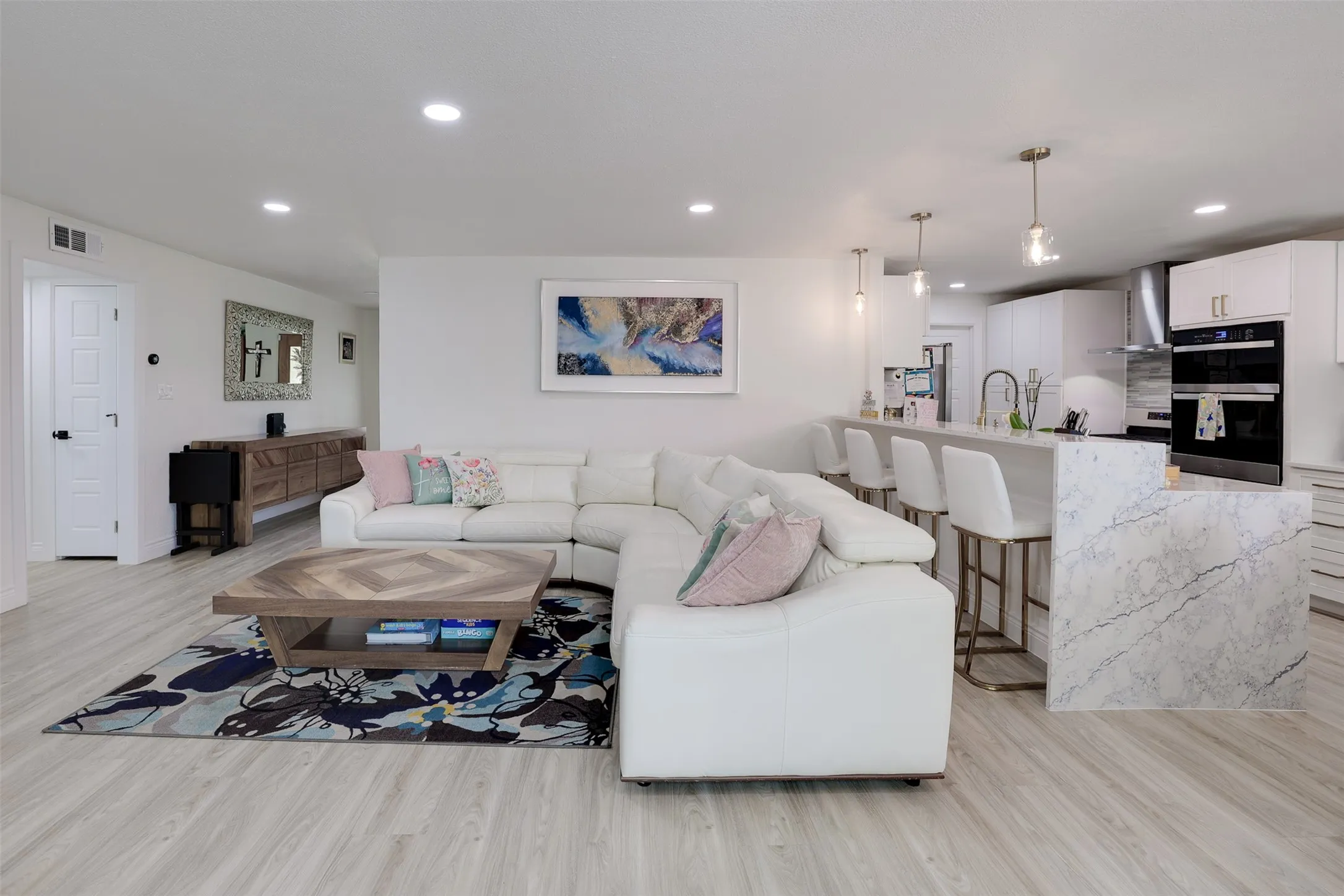 Open-concept living area featuring light wood-finish flooring, recessed lighting, and a white interior color palette