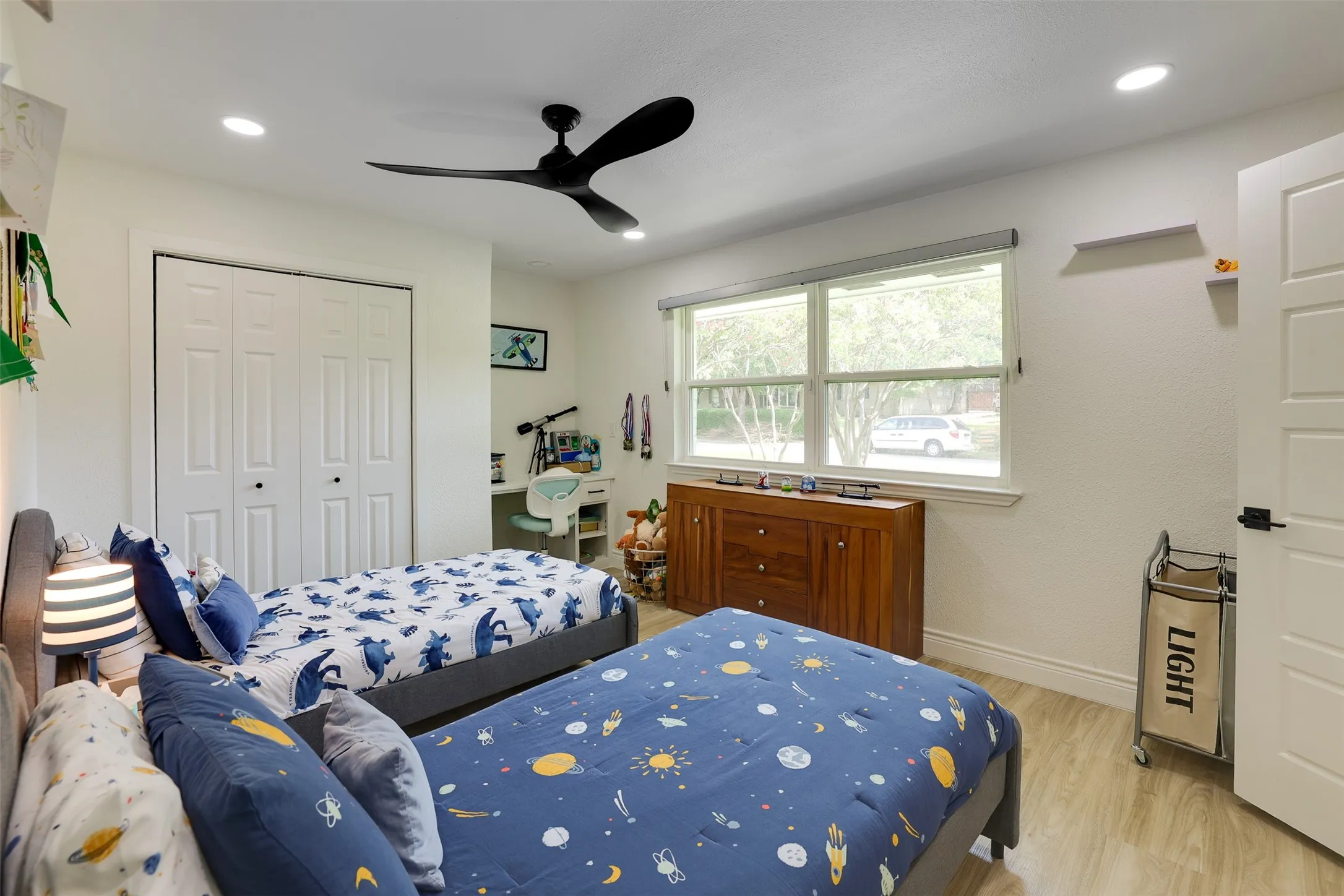 Bright room featuring a large double window, wood-finish flooring, a contemporary ceiling fan, recessed lighting, and white bi-fold closet doors