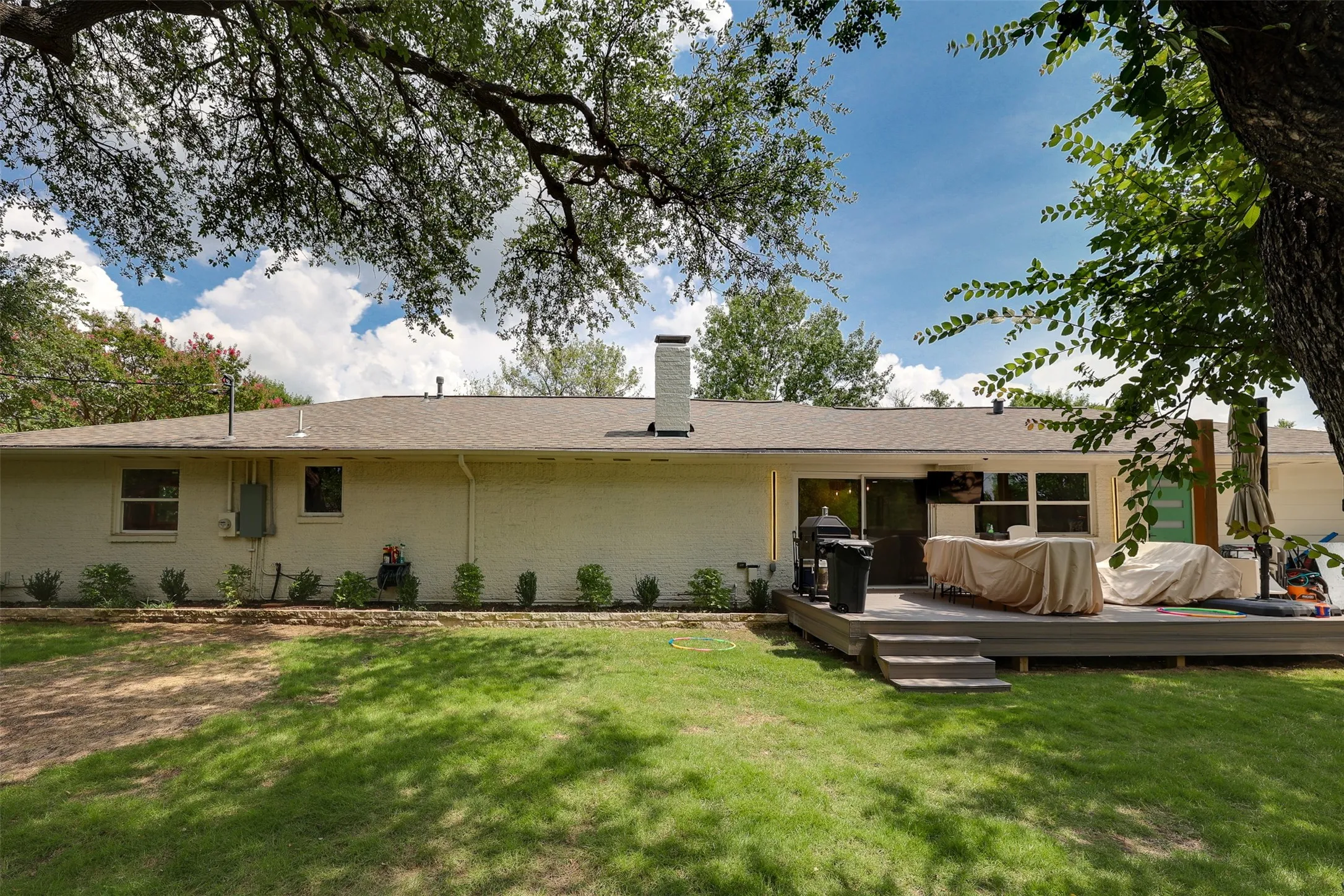 Rear exterior featuring a multi-level wood deck, sliding glass door access, and a manicured lawn