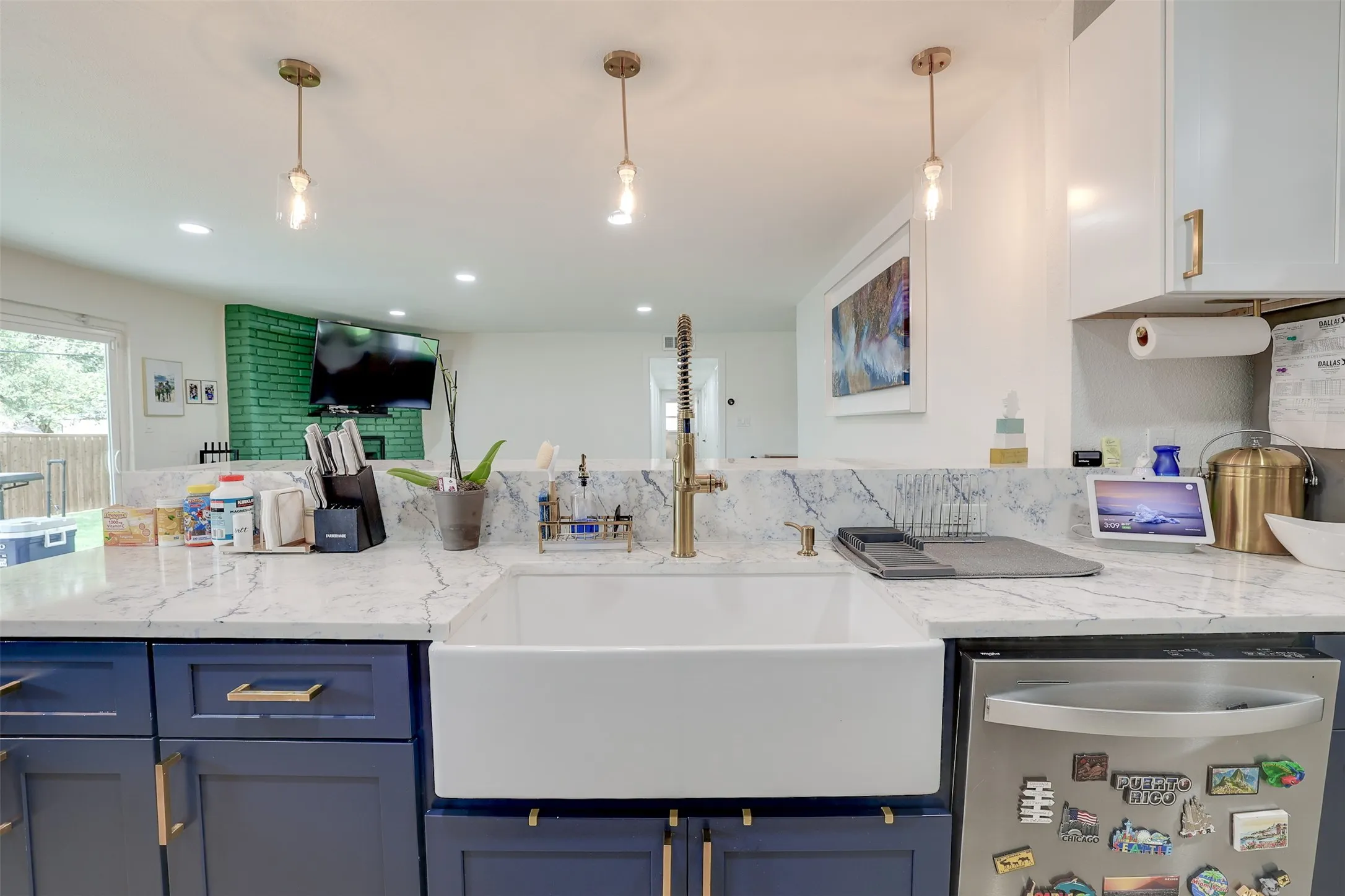 Kitchen featuring a large white farmhouse sink with a brass-finish faucet, quartz countertops, blue base cabinetry with brass-finish hardware, and a stainless steel dishwasher