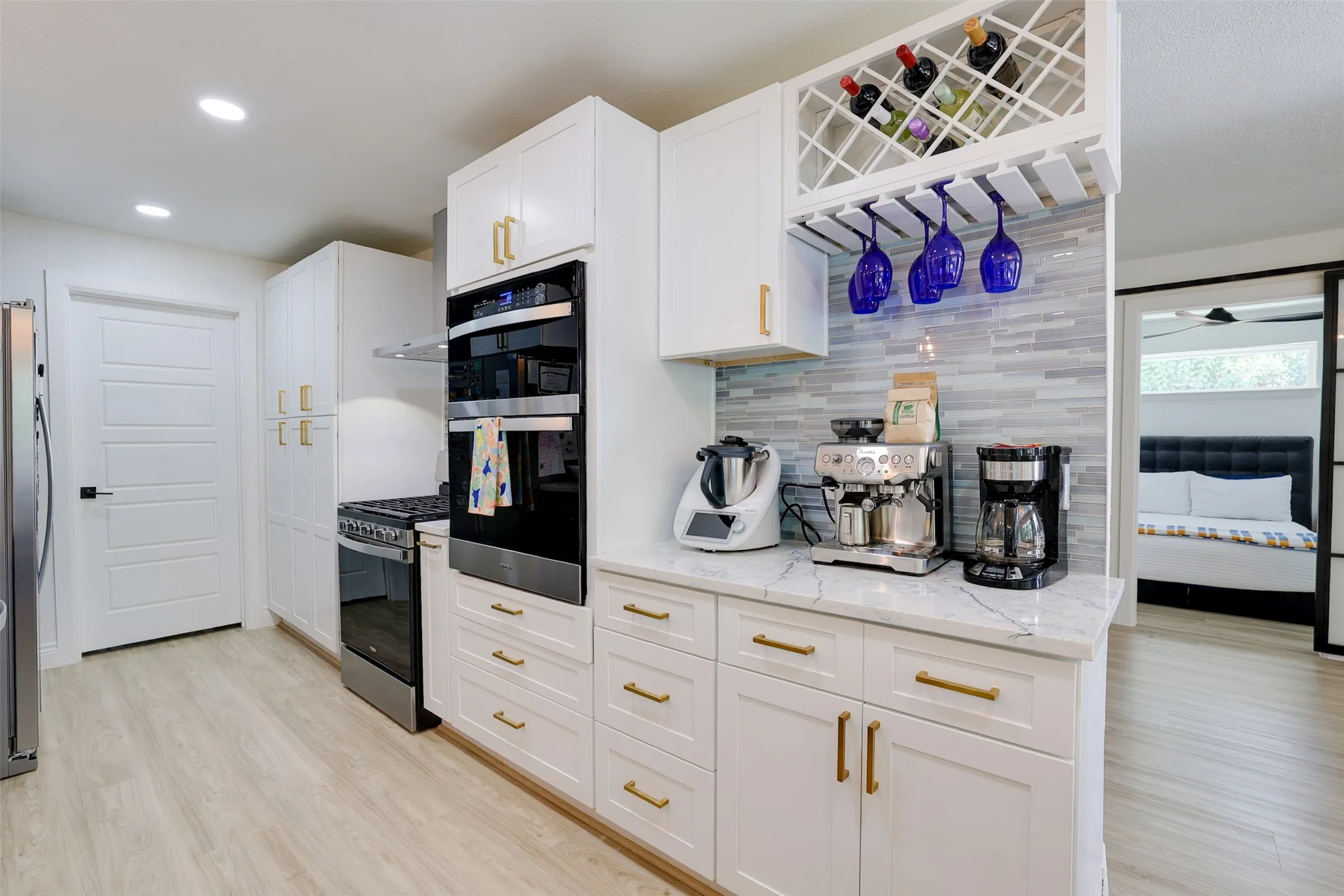 Modern kitchen featuring white cabinetry, gold-tone hardware, a light-toned wood-finish floor, and a white countertop