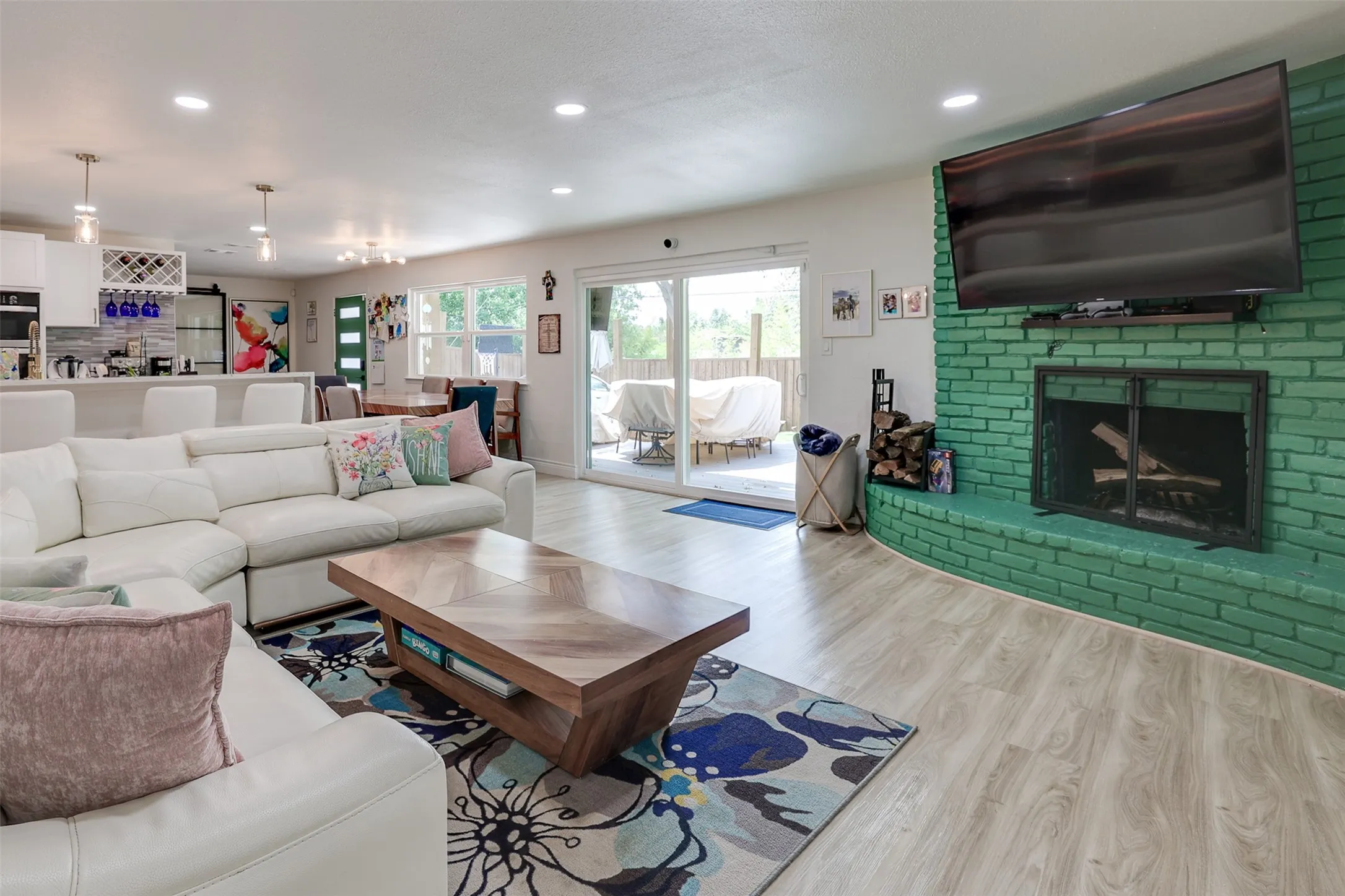 Bright living area featuring light wood-finish flooring, a painted brick fireplace, and sliding glass doors providing access to the outdoors