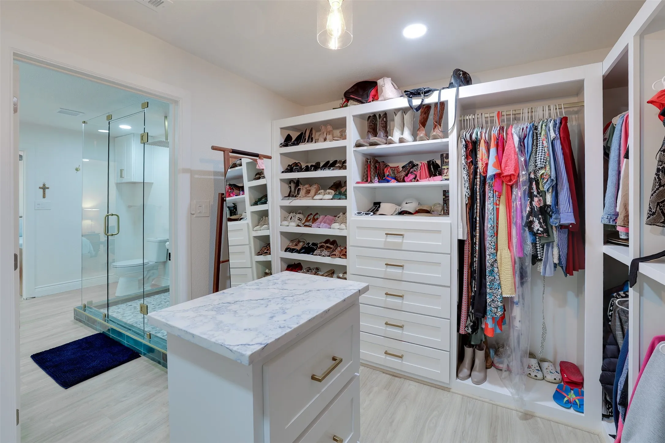 Custom closet system featuring built-in shelving and drawers, a central island with a stone-finish countertop, and light wood-finish flooring