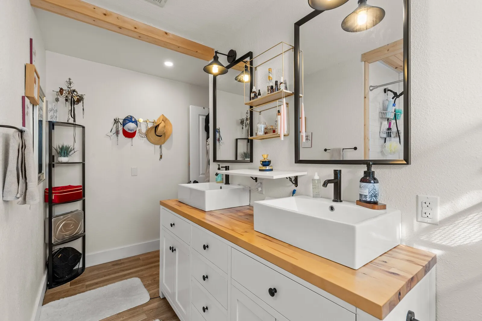 Dual vessel sinks set atop a wood-finish countertop with white cabinetry featuring dark hardware