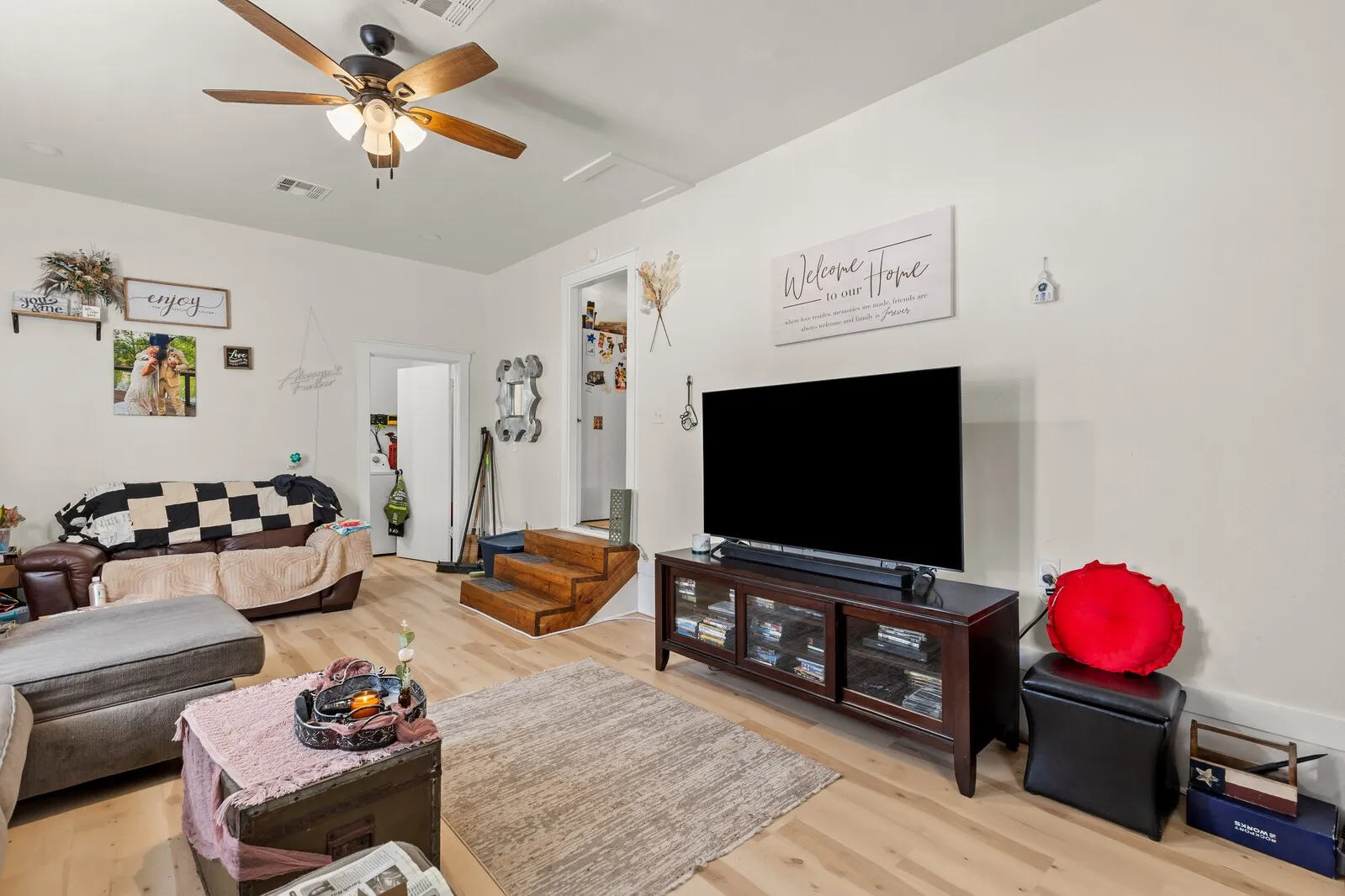 Living area featuring light wood-finish flooring, white walls, and a ceiling fan with integrated lighting