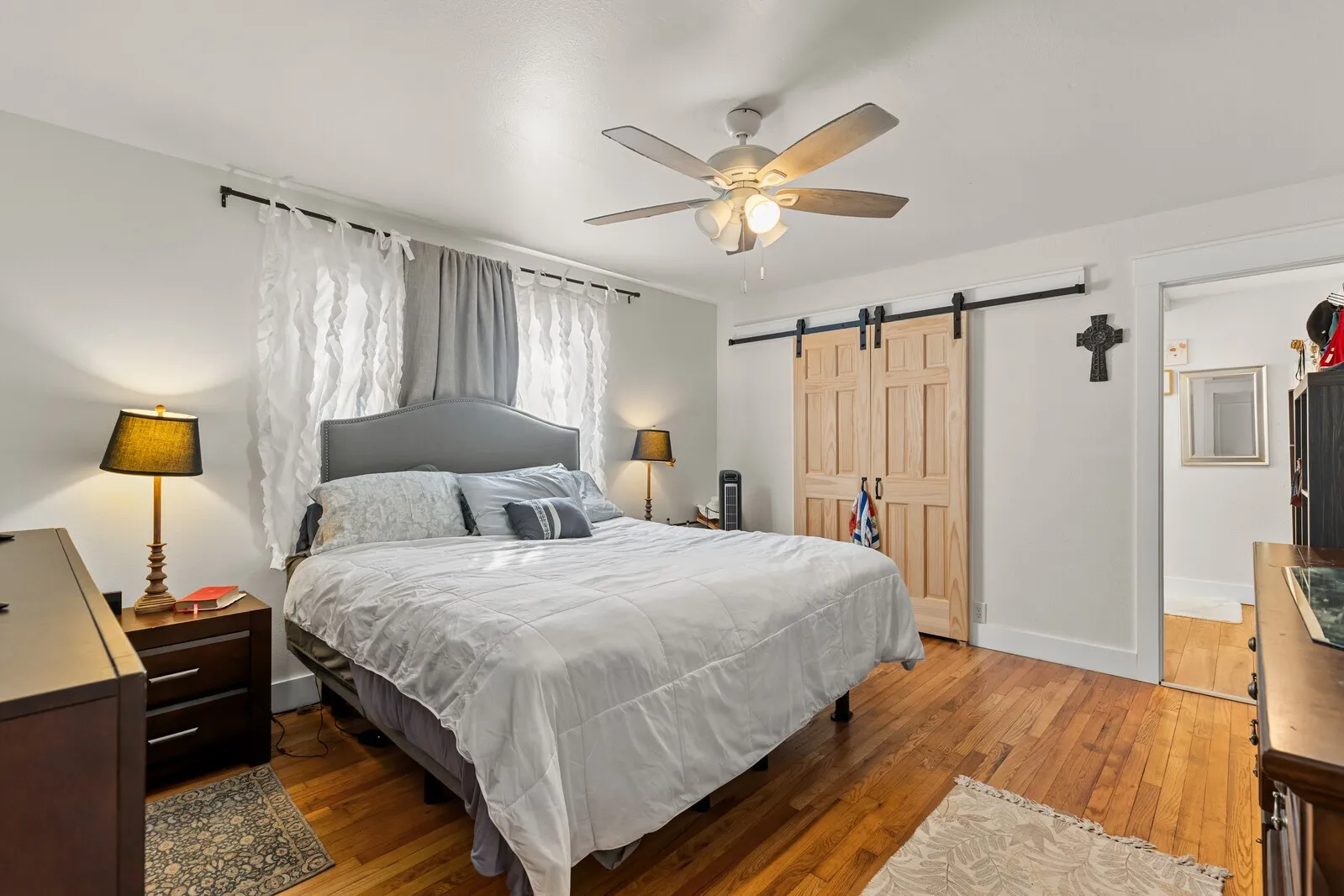 Bedroom featuring wood-finish flooring, a ceiling fan with light fixture, and a pair of barn doors on a black track