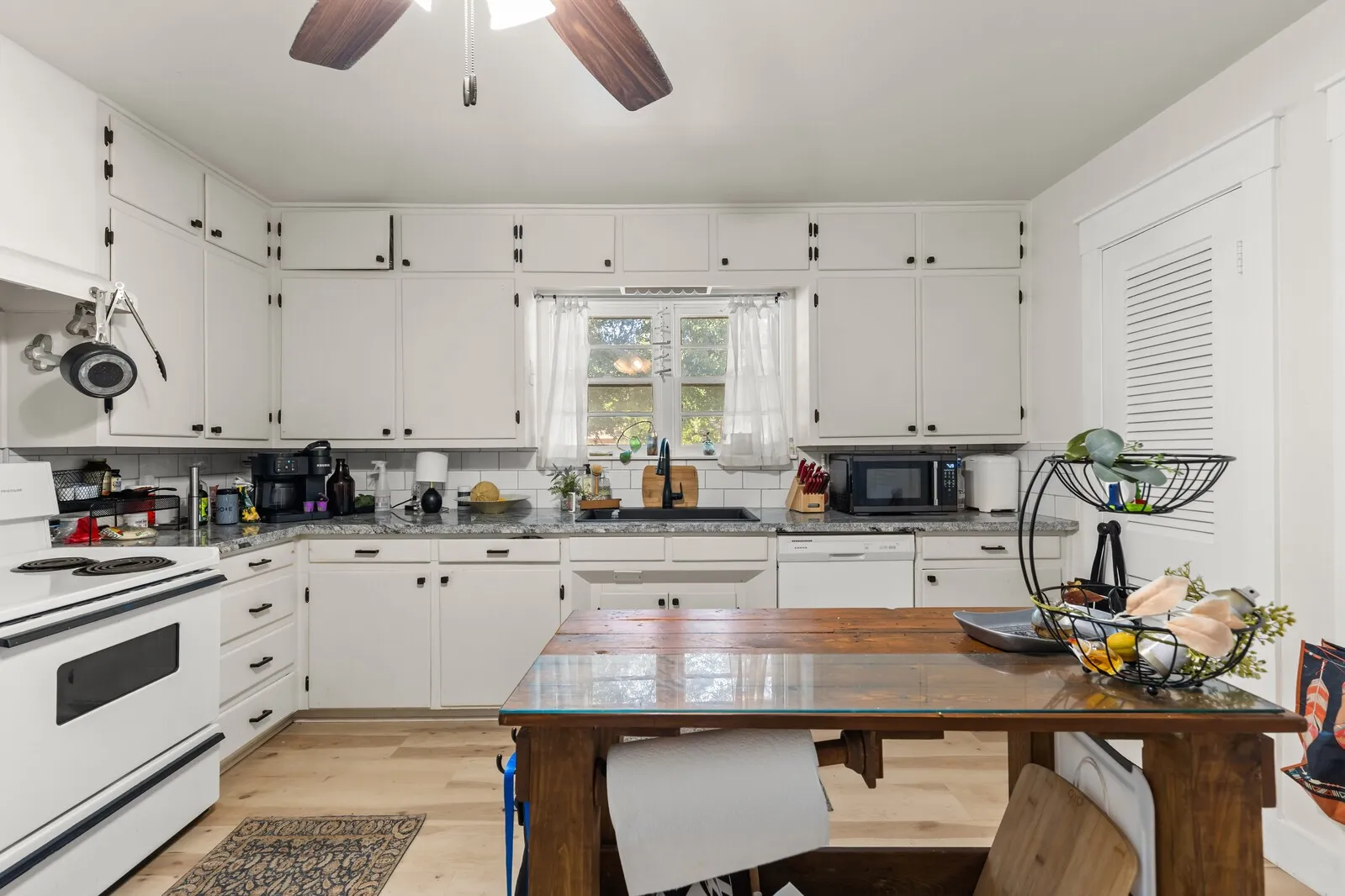 Kitchen featuring white cabinetry with black hardware, light-toned wood-finish flooring, and a window above the sink
