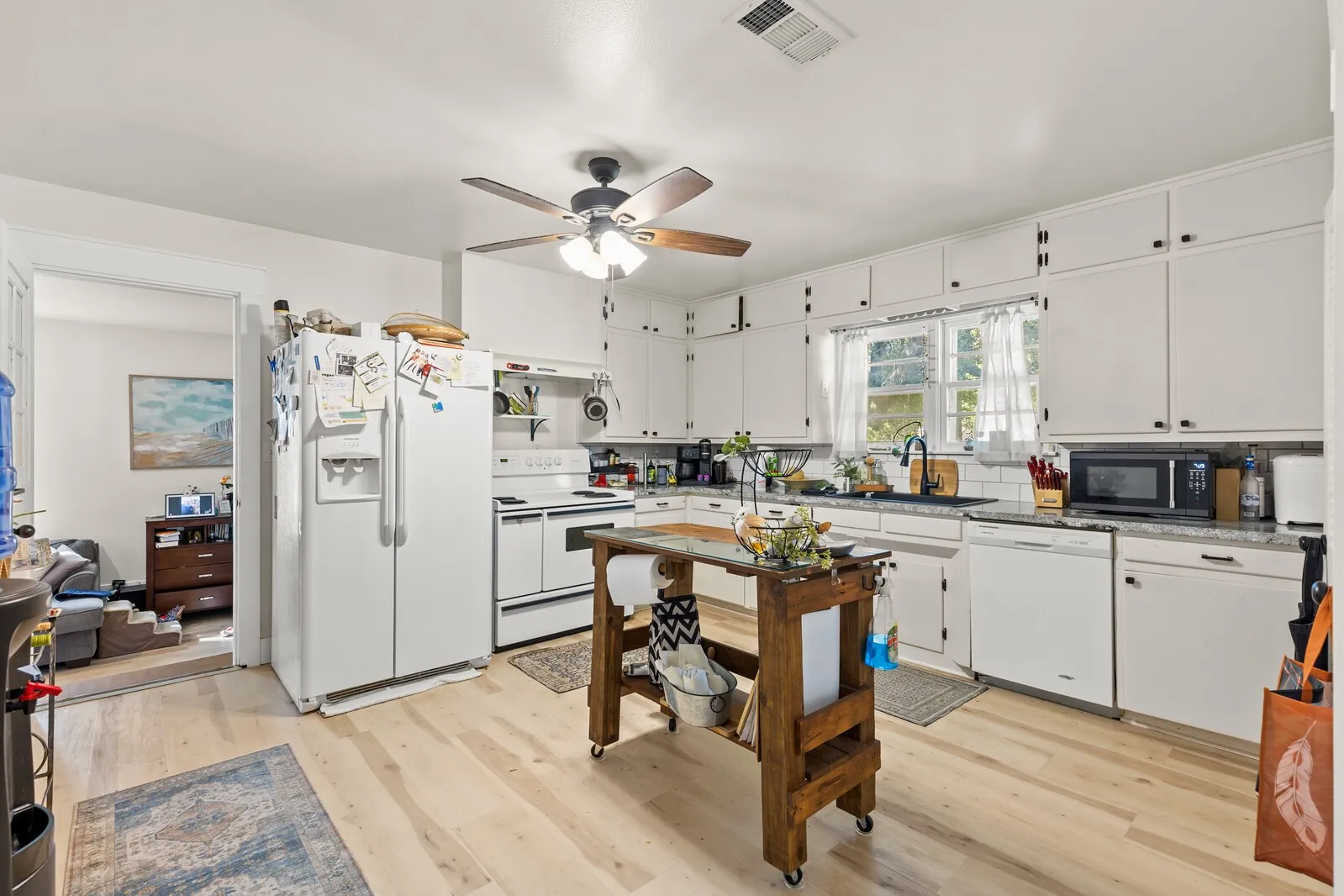 Bright kitchen featuring wood-finish flooring, white cabinetry with black hardware, a ceiling fan, and white appliances including a refrigerator, range, and dishwasher
