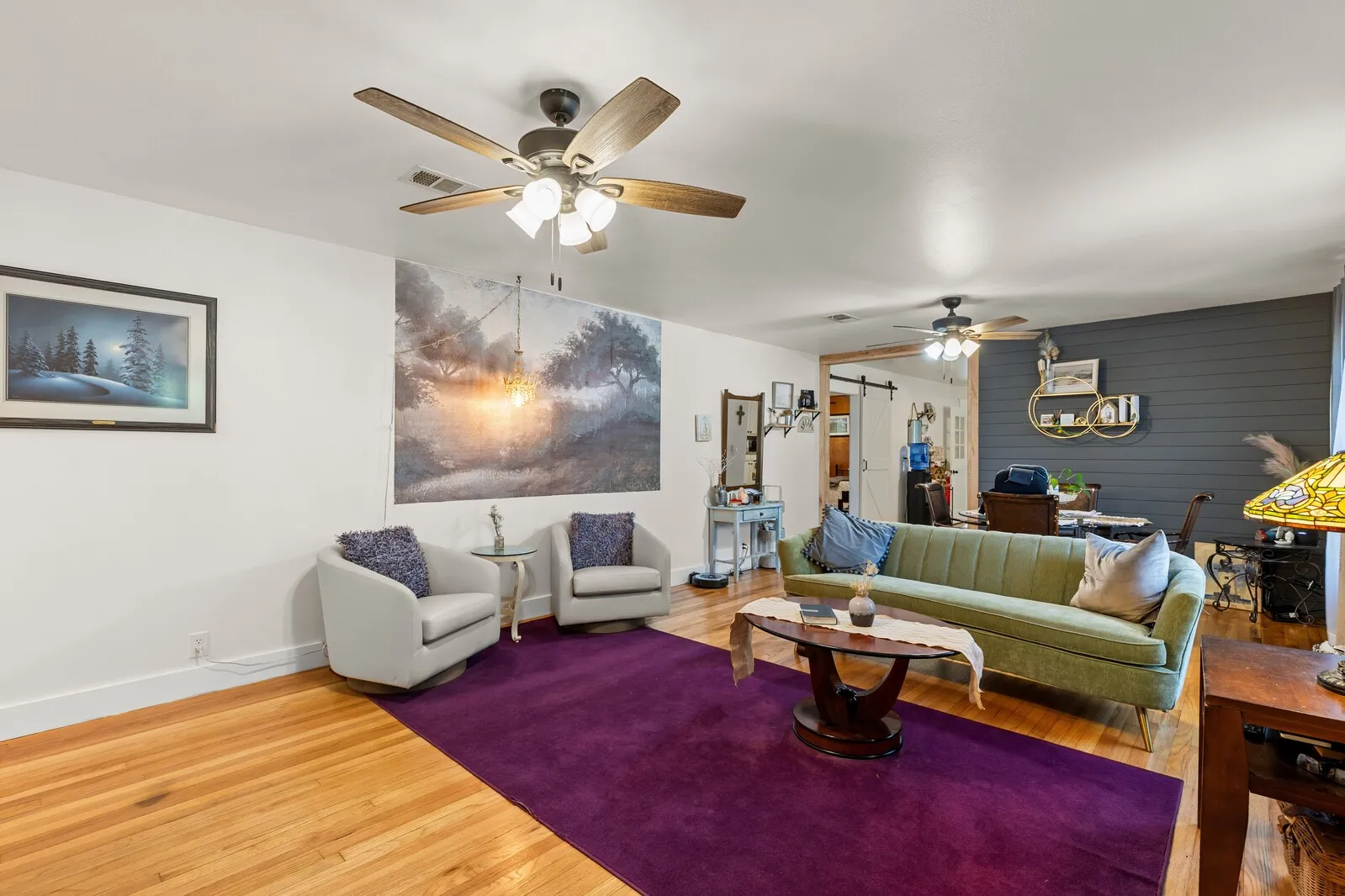Spacious living area featuring wood-finish flooring, white walls, and a ceiling fan with light fixture