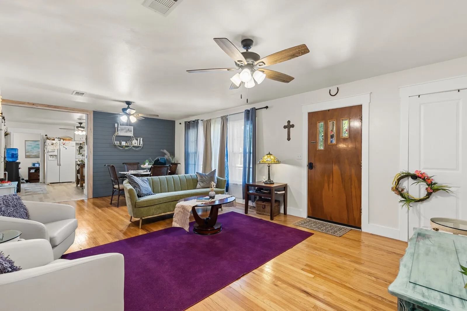 Spacious living area featuring polished wood-finish flooring, a wood-paneled accent wall, and multiple ceiling fans