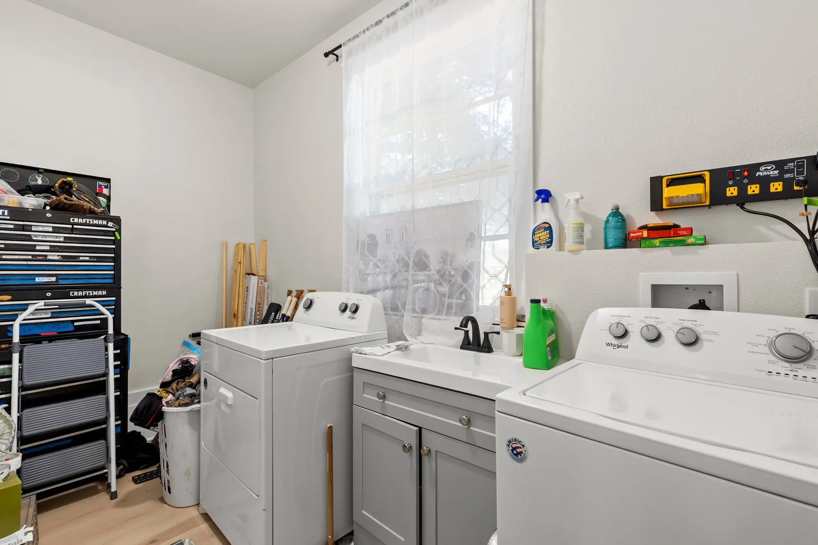 Functional utility room with light-toned walls, a sink with a dark-finish faucet, and a lower cabinet with light gray doors