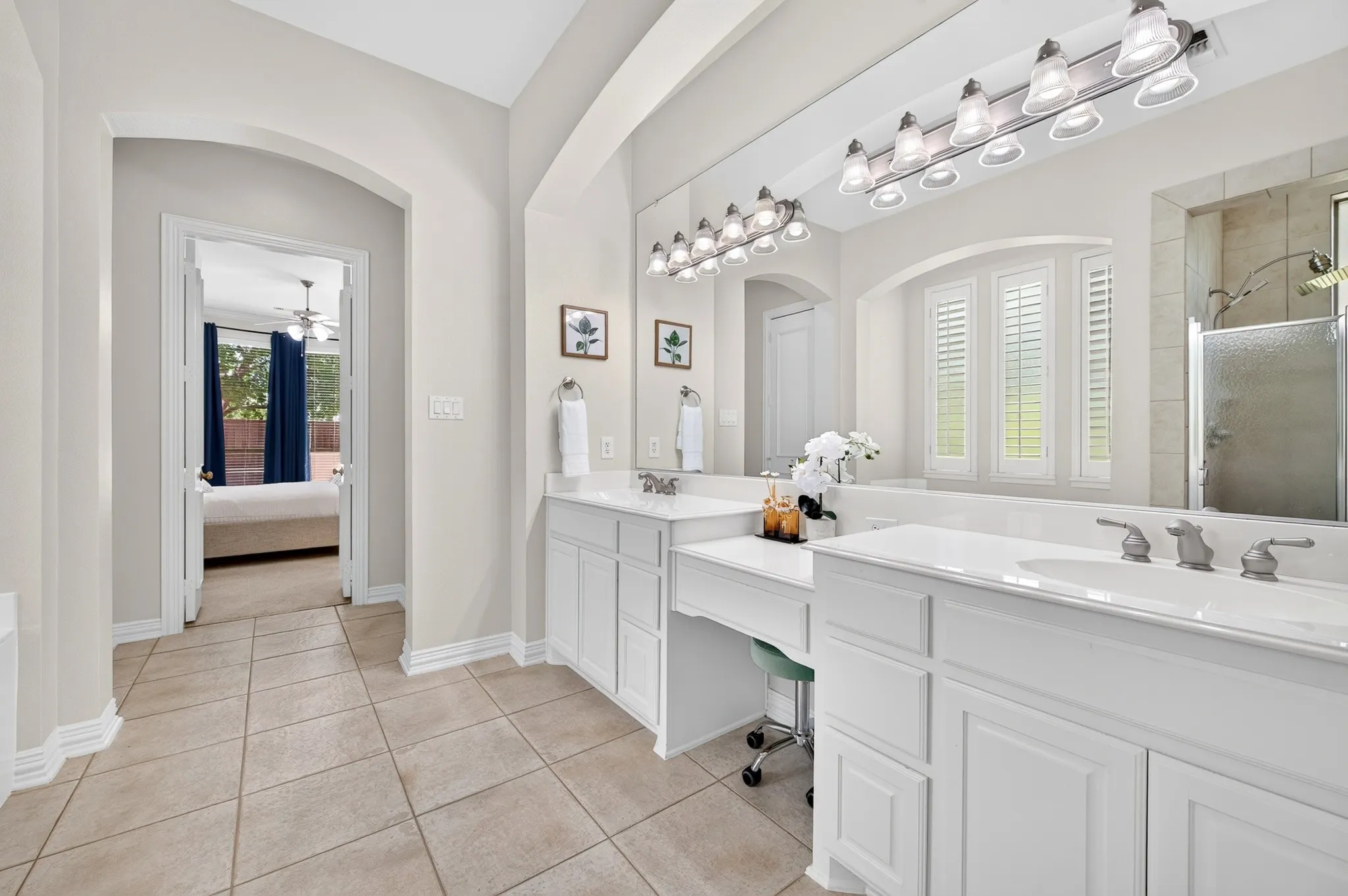 Bathroom featuring dual vanities with white cabinetry, a built-in vanity desk, a large mirror, and tiled flooring