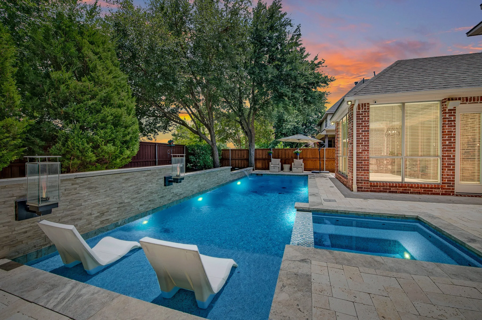 Contemporary swimming pool featuring integrated spa, tiled water line, and stone-clad retaining wall with wall-mounted lighting