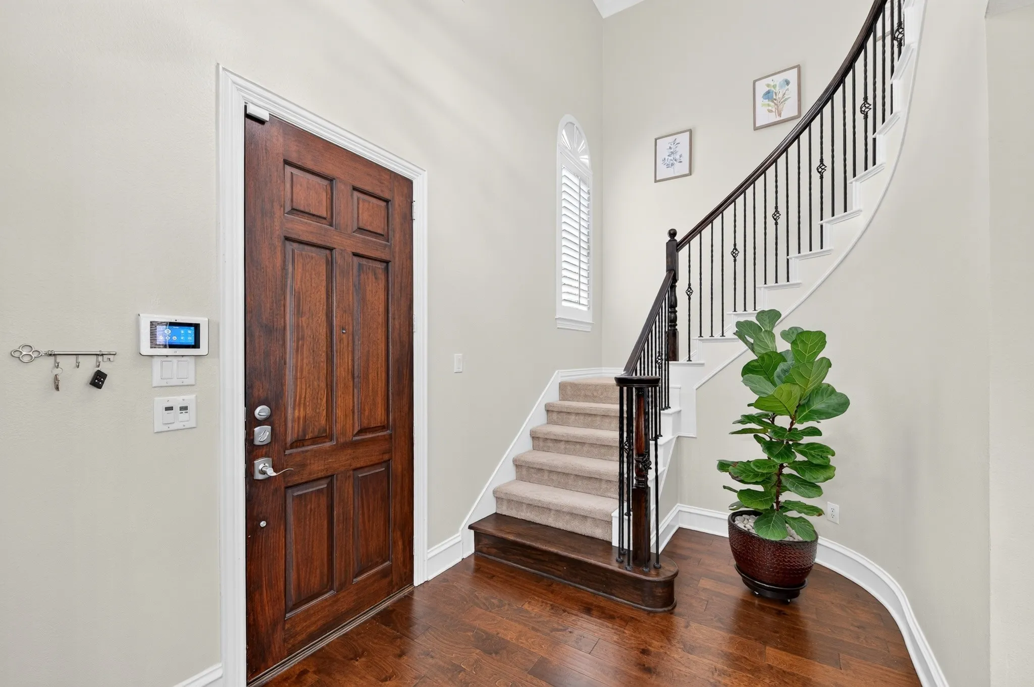 Grand entry with rich wood-finish flooring and a curved staircase featuring wrought iron balusters