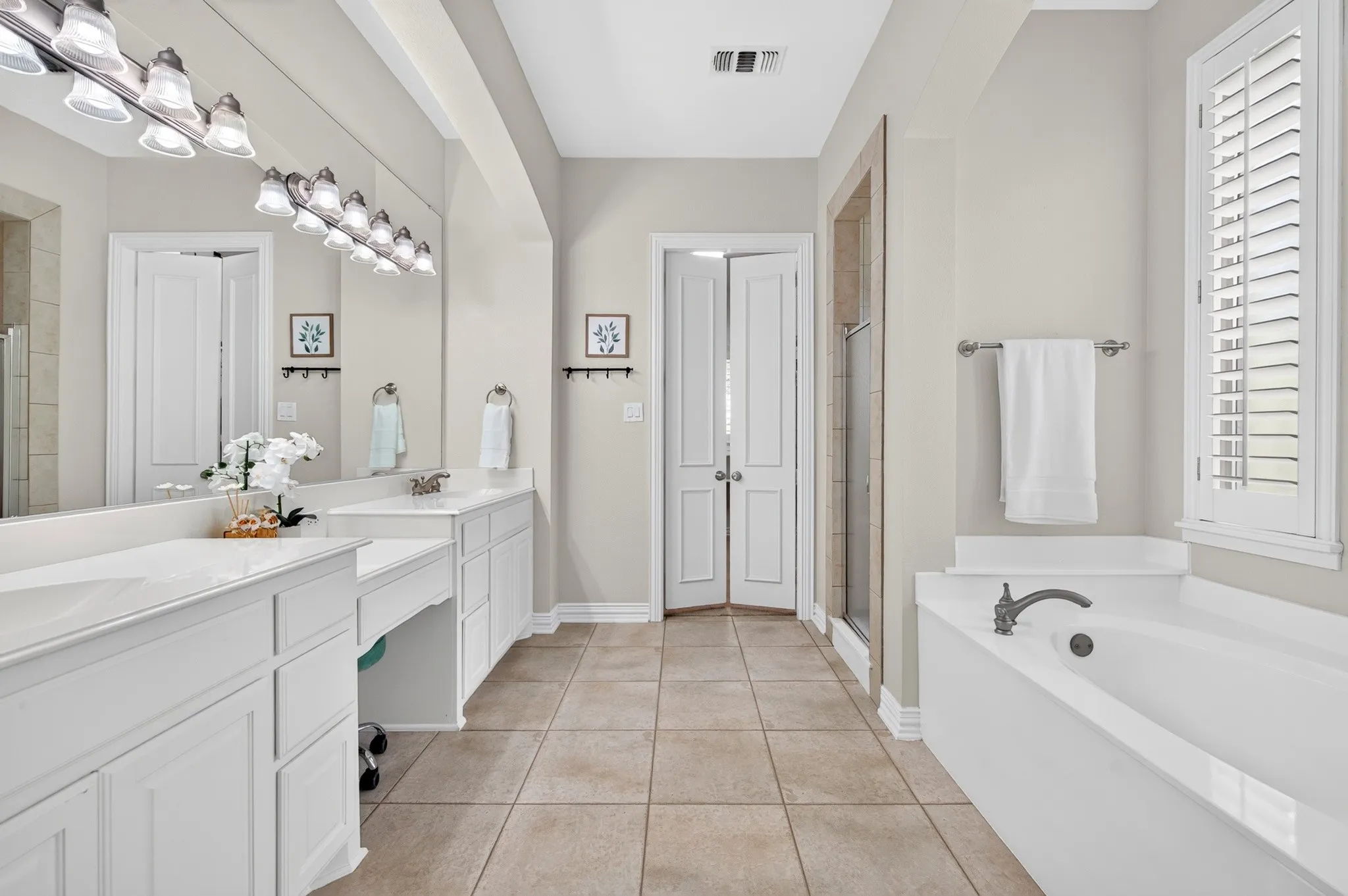 Spacious bathroom featuring dual vanities with white cabinetry, ample counter space, and integrated sinks