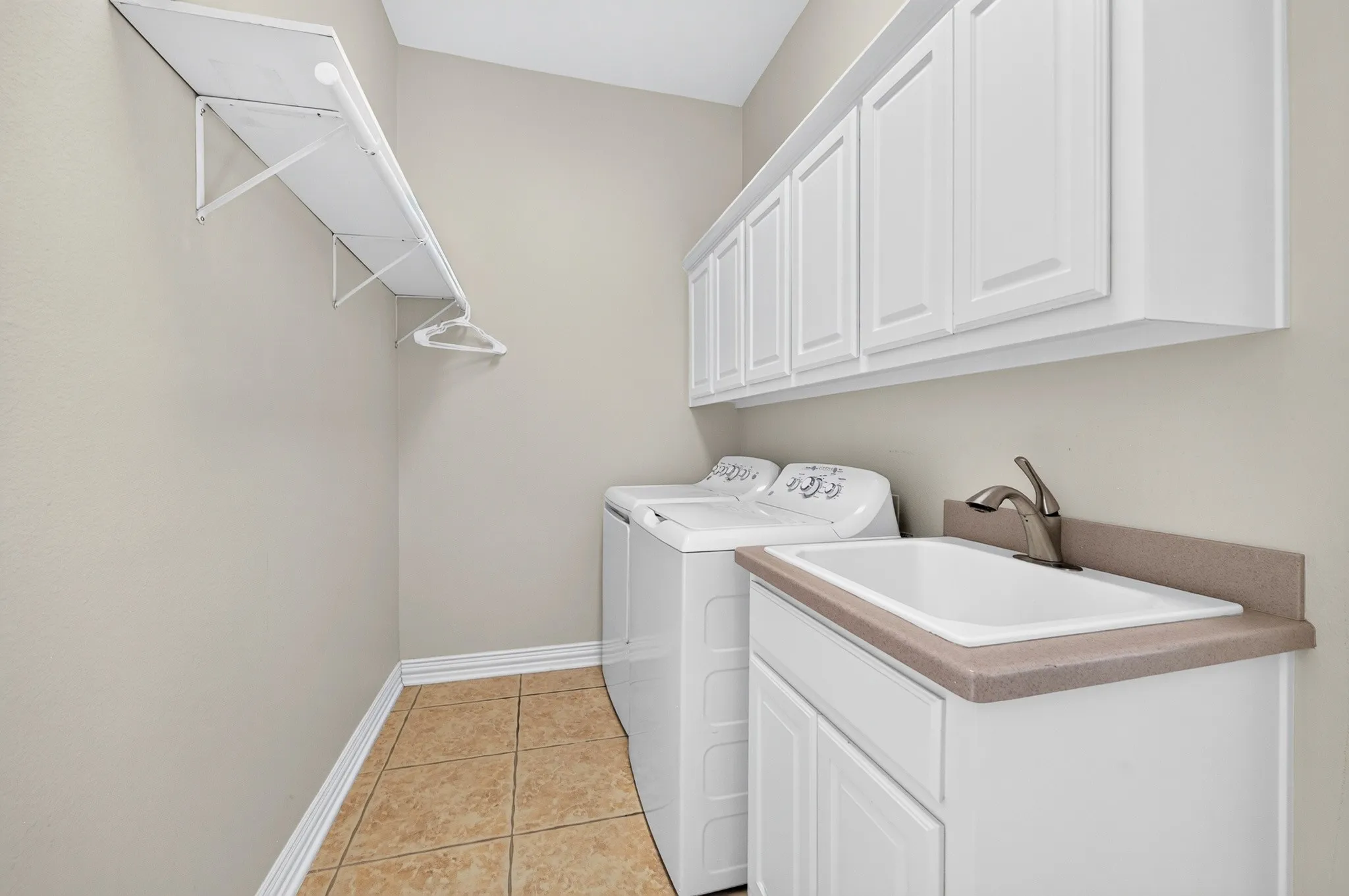 Laundry area featuring tiled flooring, a utility sink with a brushed nickel faucet, white shaker-style cabinetry, and a wall-mounted shelving unit