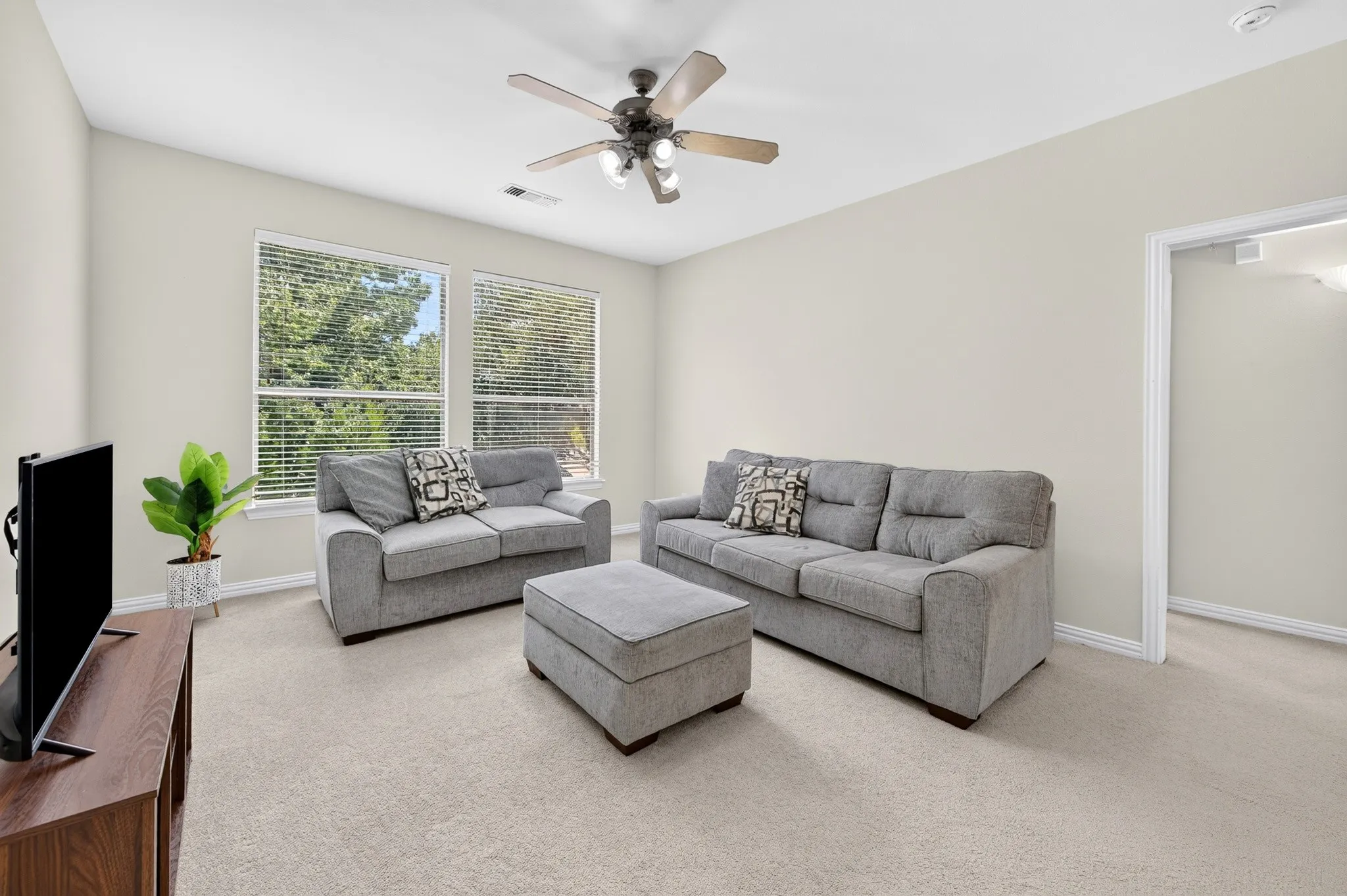 Carpeted room with multiple windows offering natural light, a ceiling fan, neutral wall paint, and white trim