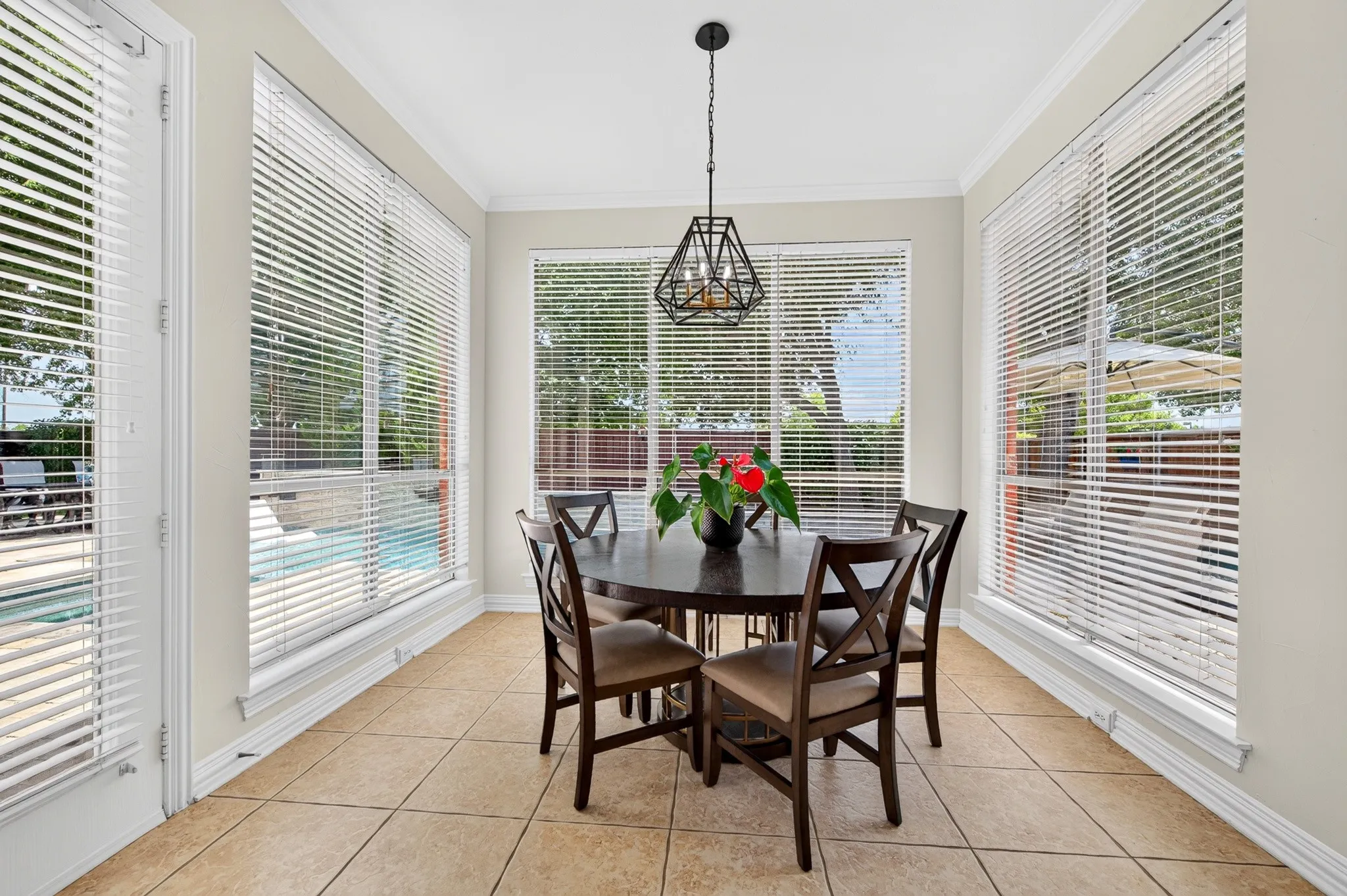 Bright dining area featuring large windows with horizontal blinds, tiled flooring, and a modern geometric pendant light fixture