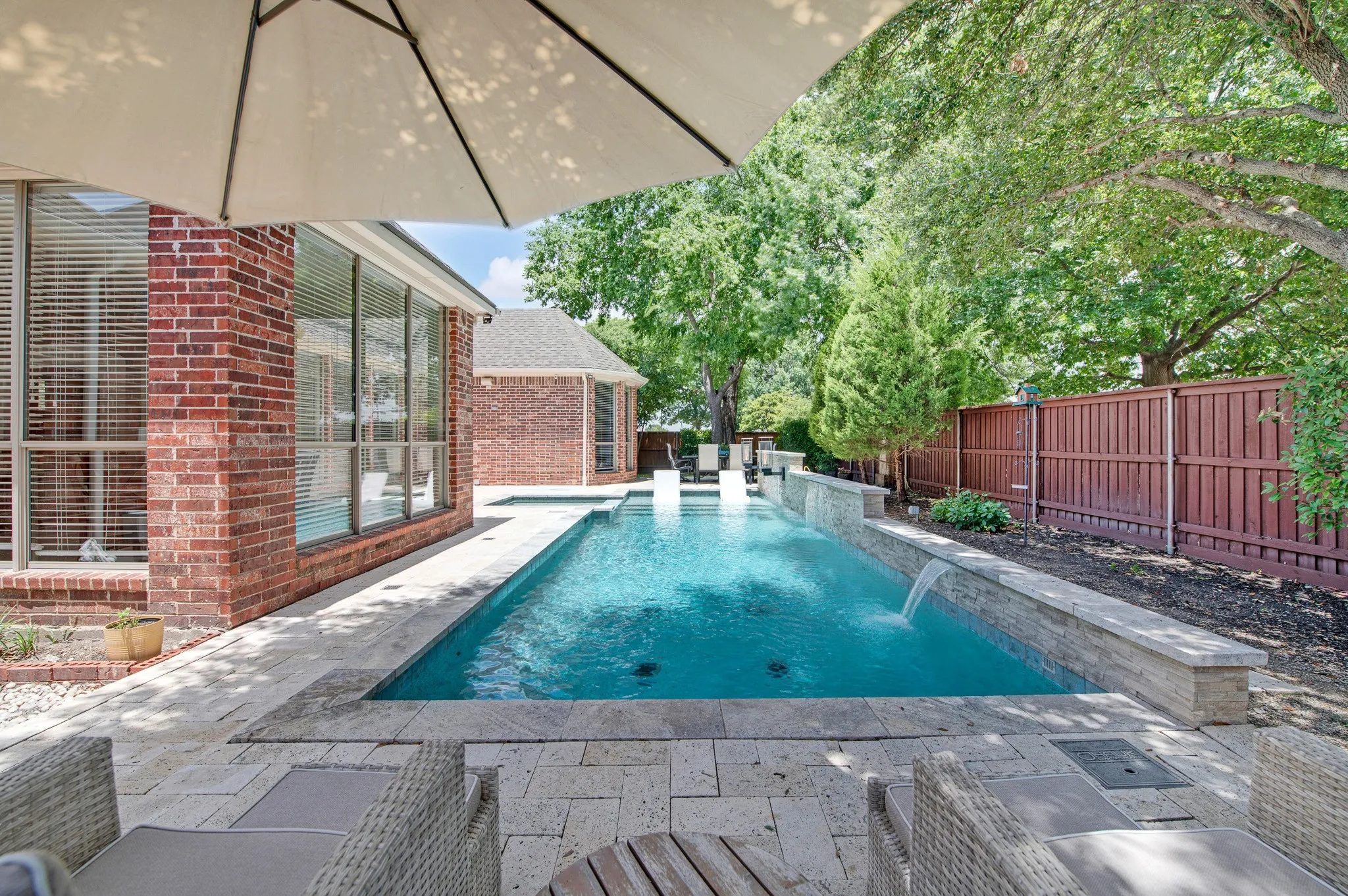 Outdoor swimming pool featuring a waterfall, integrated seating, and a stone-clad raised planter