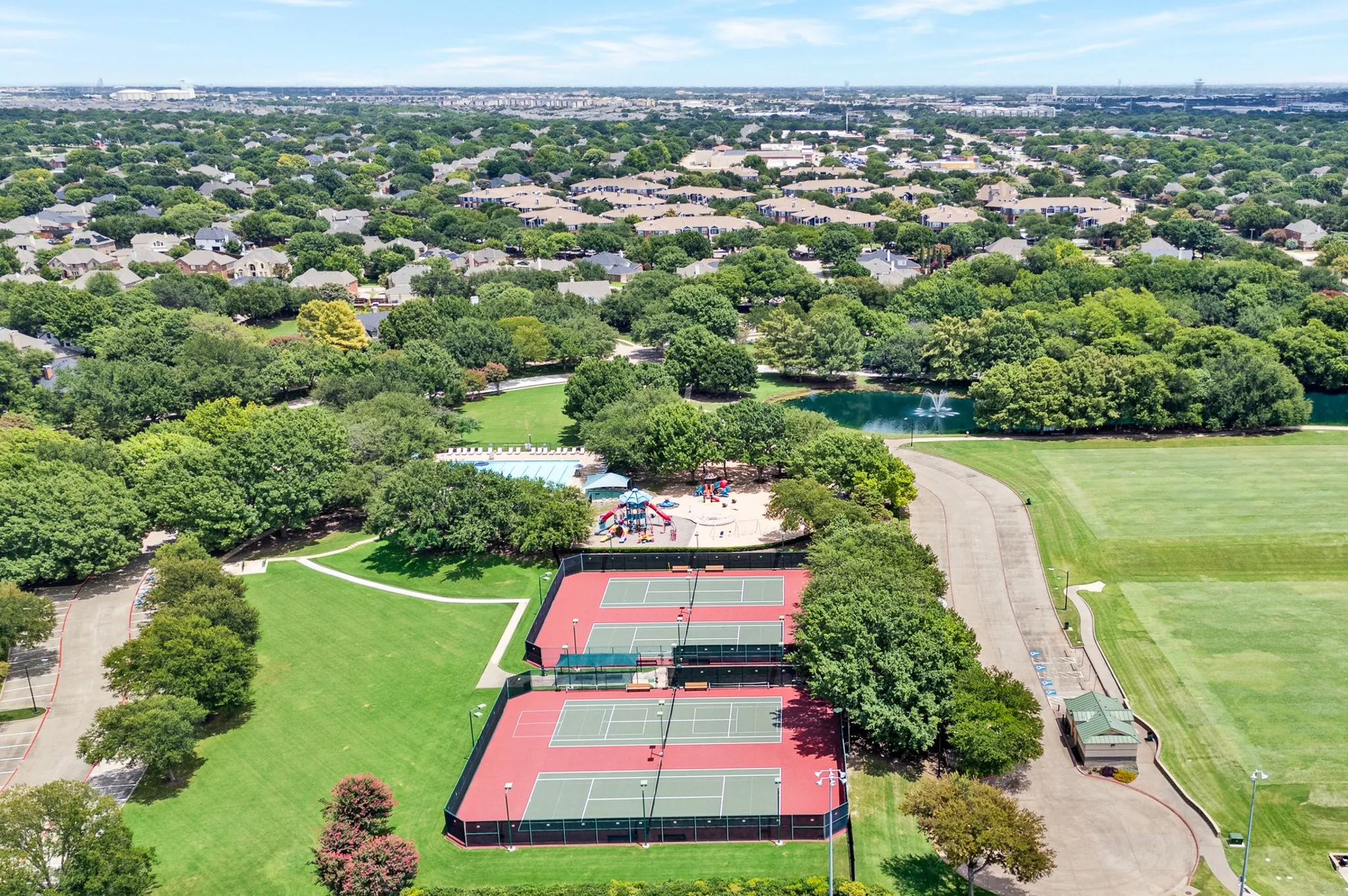 Aerial perspective showcasing multiple red-surfaced tennis courts, a swimming pool area, and a playground