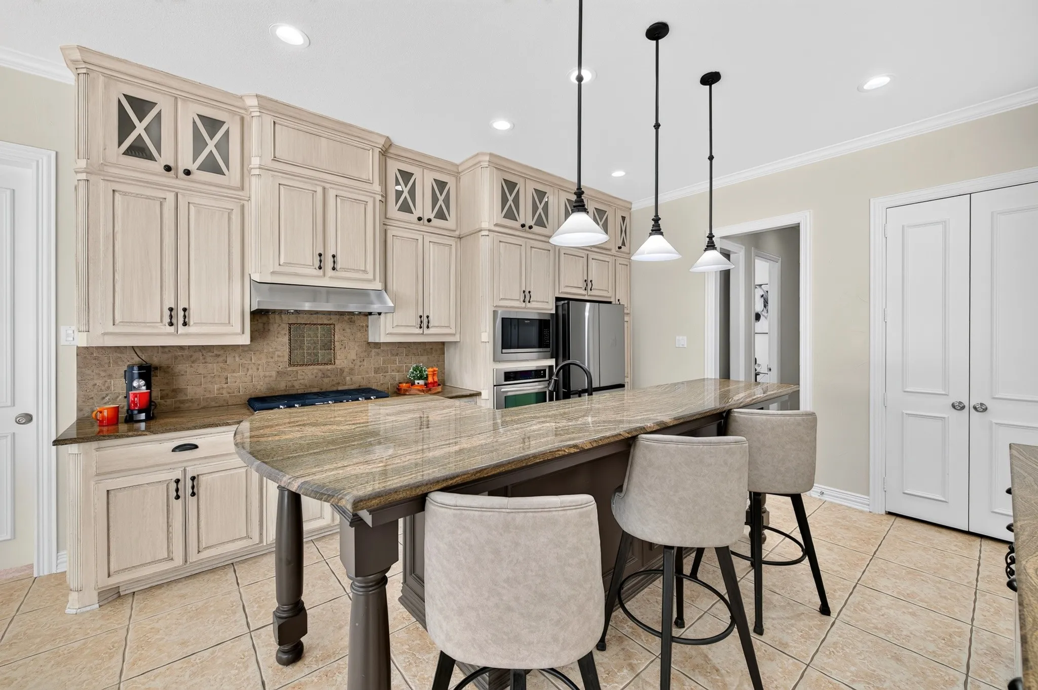Kitchen featuring a large island, pendant lighting, built-in stainless steel appliances, extensive cabinetry, and tile flooring
