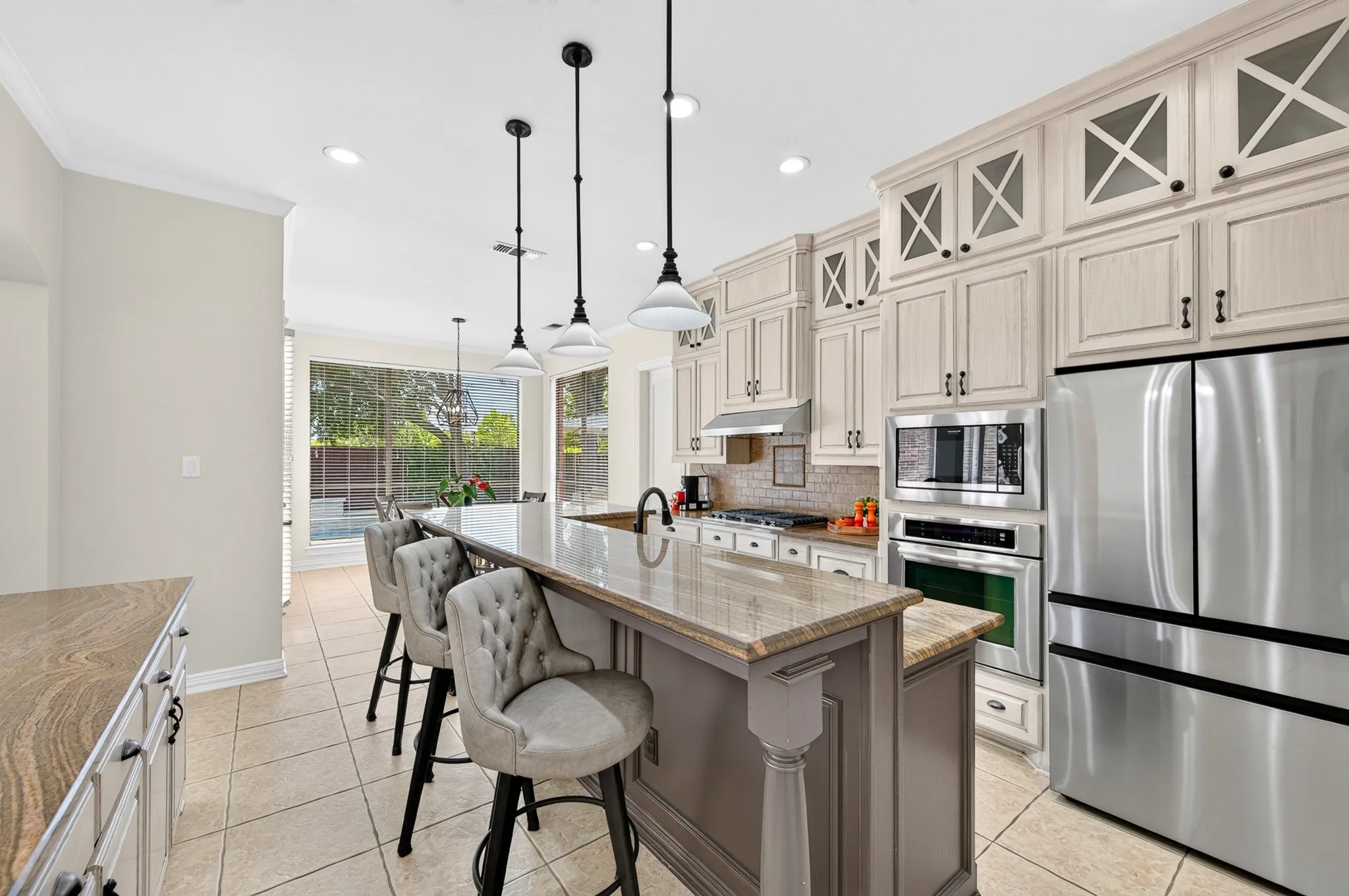 Spacious kitchen featuring a large central island with a stone countertop, extensive cabinetry with decorative glass inserts, and stainless steel appliances