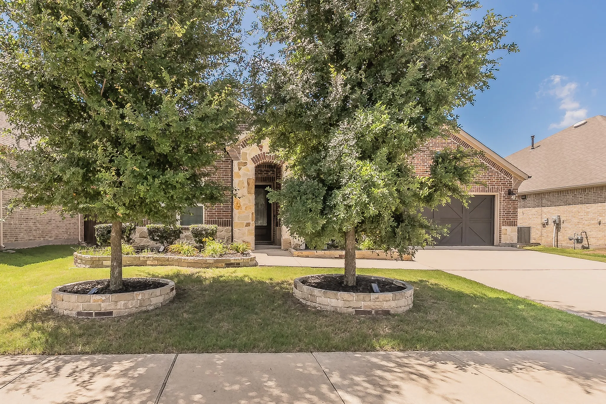 Brick and stone facade featuring an arched entryway, a concrete driveway, and a two-car garage with decorative doors