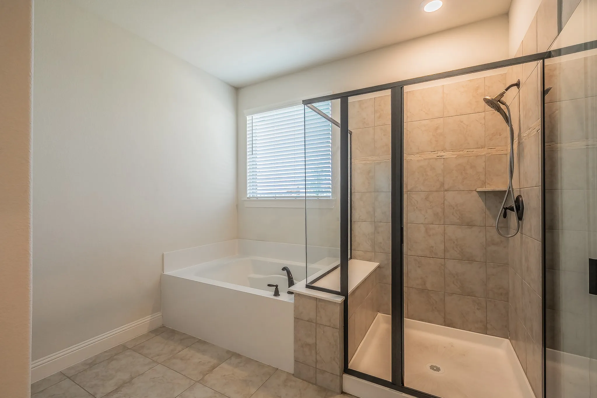 Spacious bathroom featuring a built-in tub with matte black fixtures, a separate glass-enclosed shower with tiled walls, and a window with blinds
