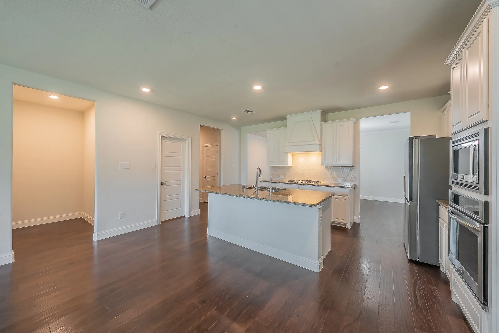 Gourmet kitchen featuring a central island with a double basin sink, light-toned granite countertops, white cabinetry, stainless steel appliances, and wood-finish flooring