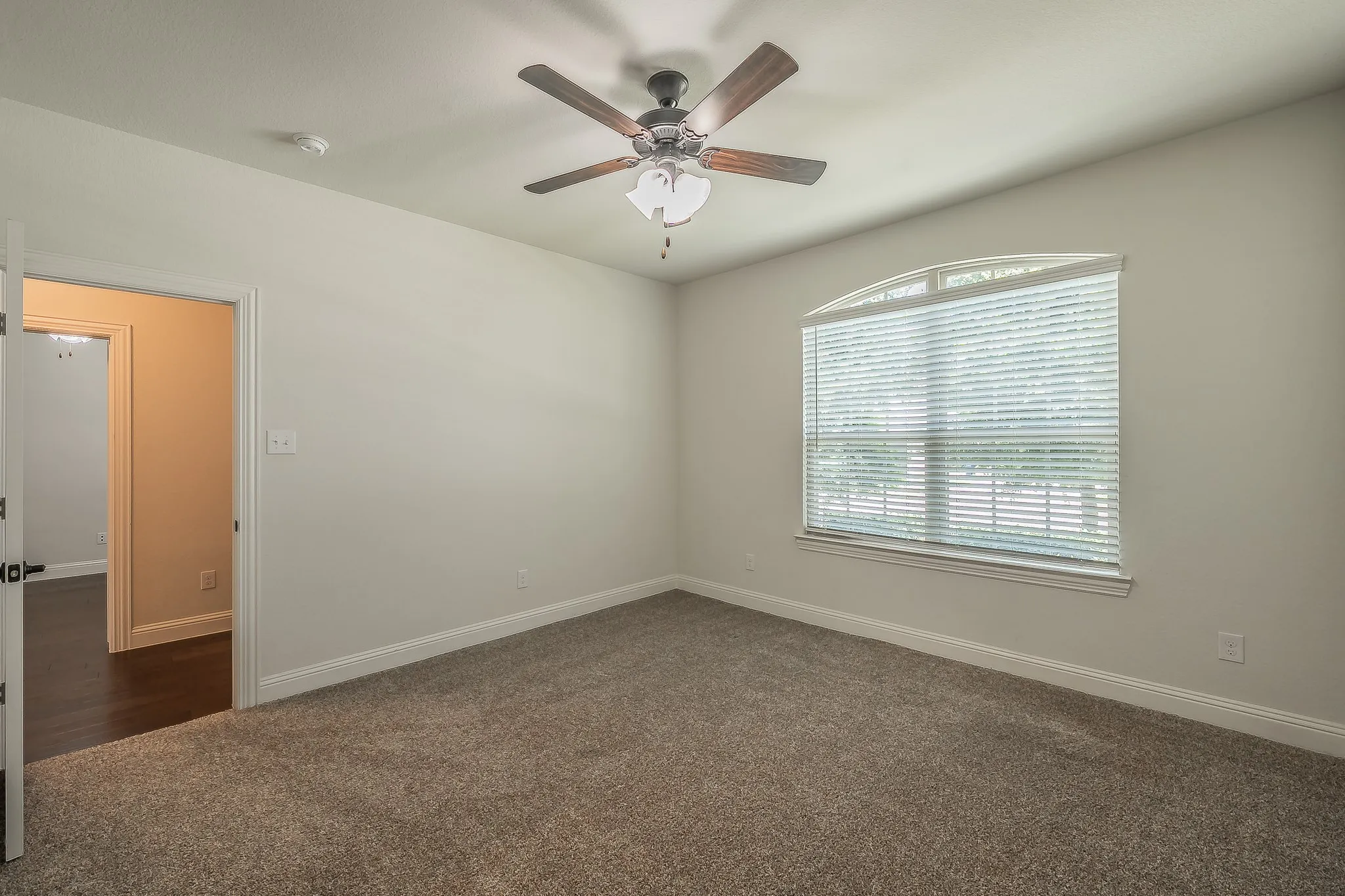 Neutral-toned room featuring a vaulted ceiling with a ceiling fan, arched window with horizontal blinds, and plush carpet flooring