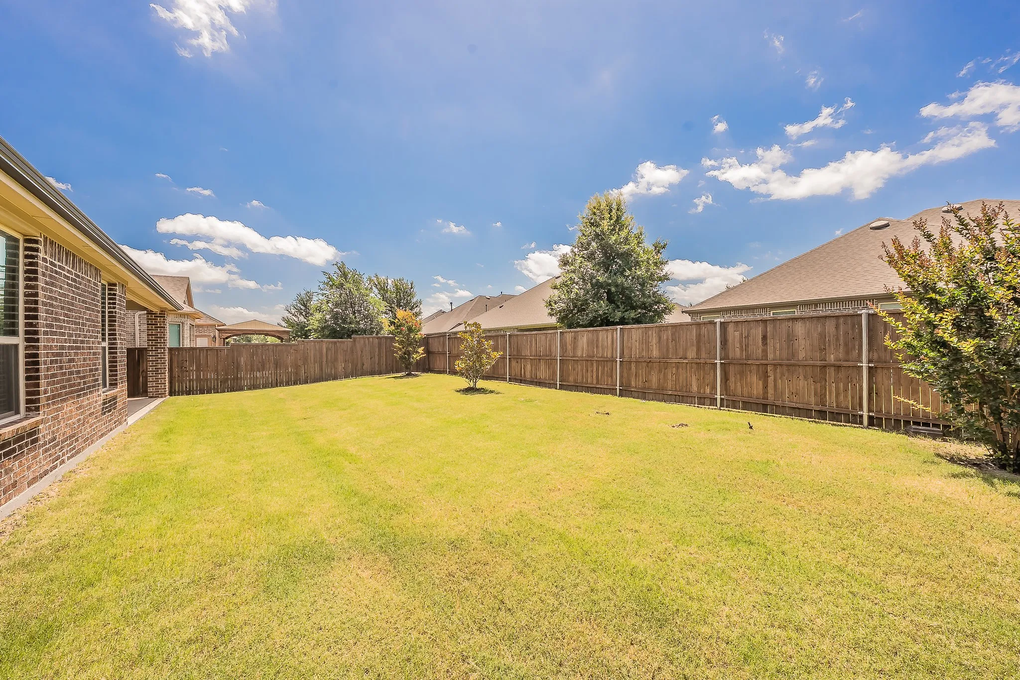 Expansive backyard featuring a manicured lawn, a full privacy fence, and mature landscaping