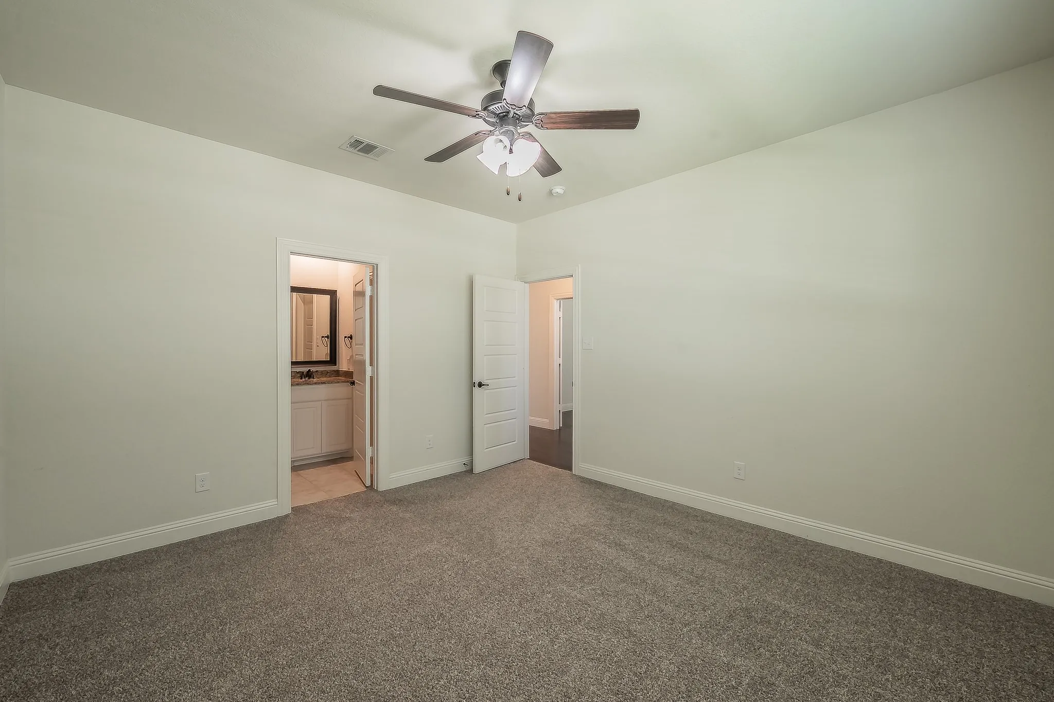 Spacious room featuring neutral carpeting, a ceiling fan with light fixture, and light-colored walls