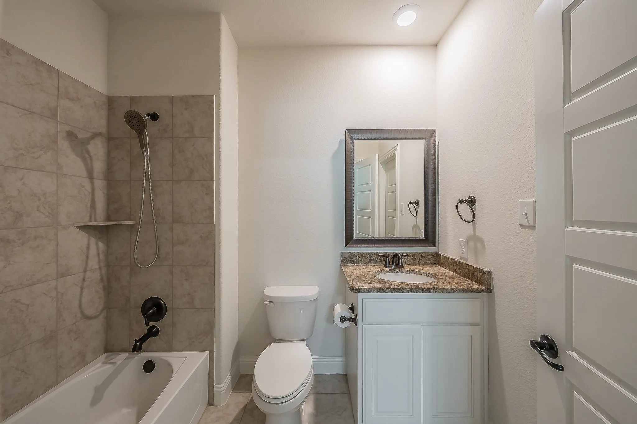 Bathroom featuring a white bathtub, a tiled shower surround, a toilet, a vanity with a granite-style countertop, and a framed mirror